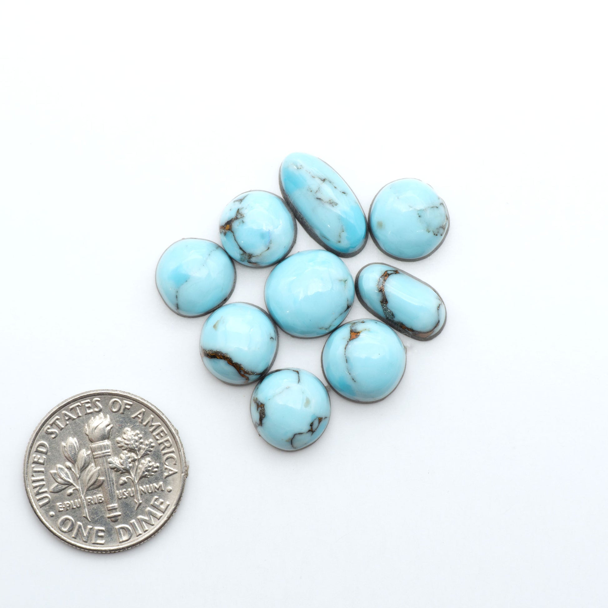 Pressed Turquoise nugget cabochons, composite material with a blue color and dark matrix on a white background, with a US dime for scale.