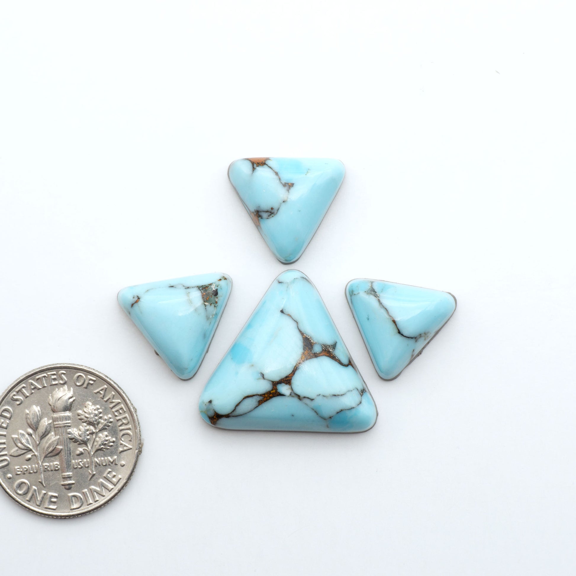 Pressed Turquoise nugget cabochons, composite material with a blue color and dark matrix on a white background, with a US dime for scale.