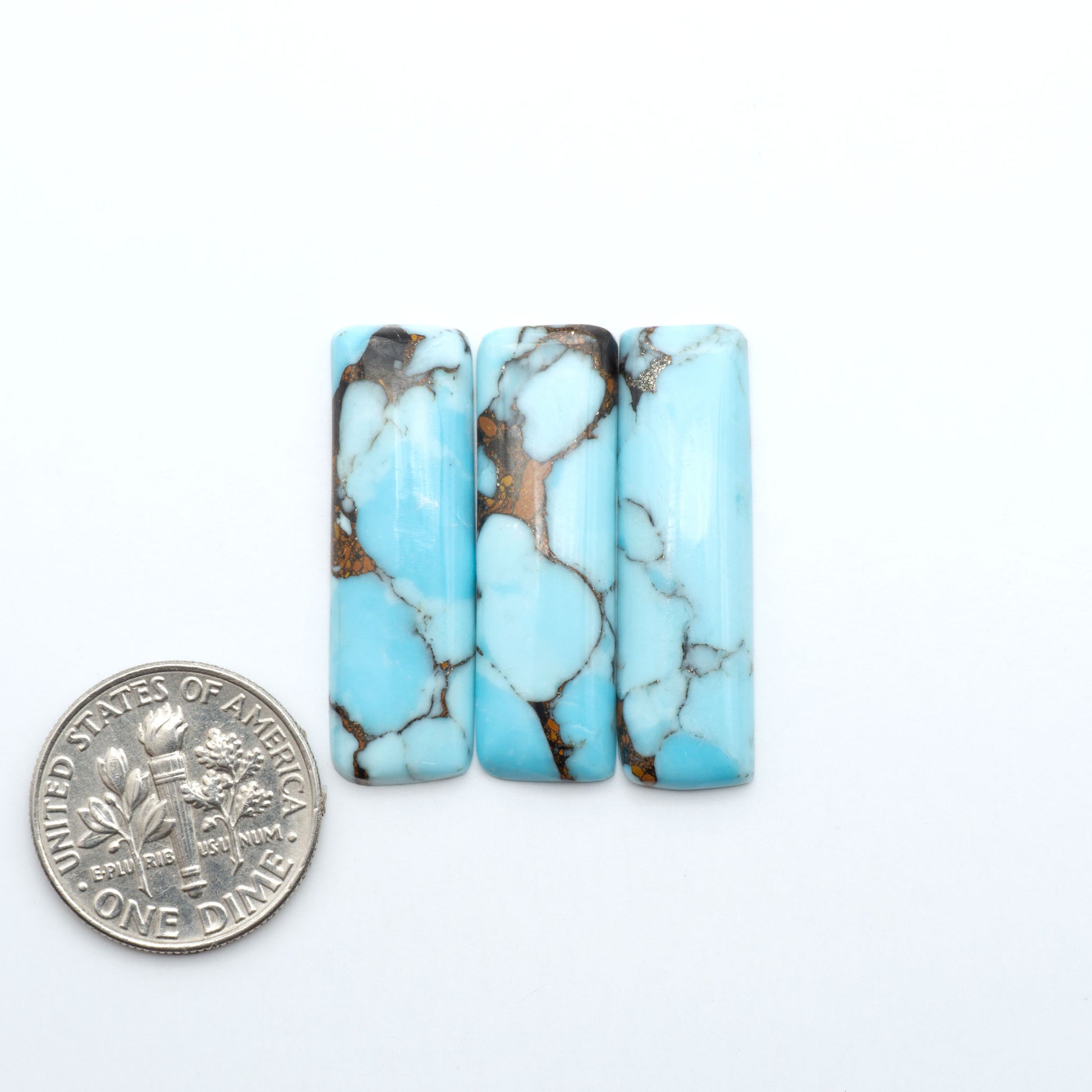 Pressed Turquoise nugget cabochons, composite material with a blue color and dark matrix on a white background, with a US dime for scale.