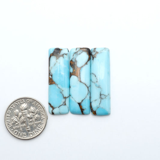 Pressed Turquoise nugget cabochons, composite material with a blue color and dark matrix on a white background, with a US dime for scale.