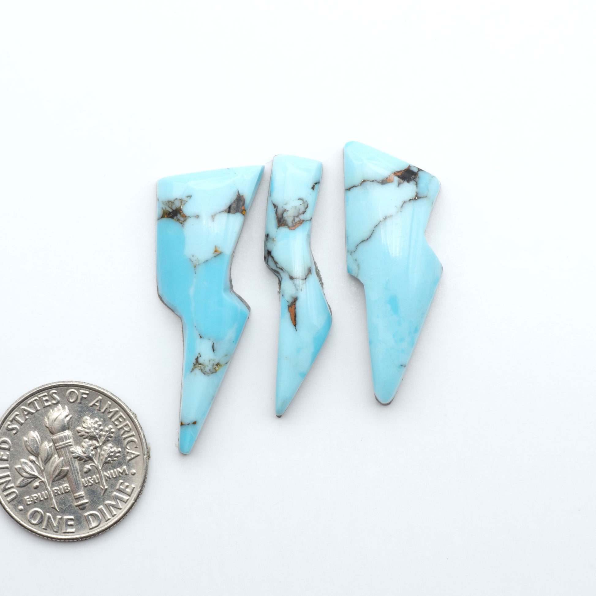 Pressed Turquoise nugget cabochons, composite material with a blue color and dark matrix on a white background, with a US dime for scale.