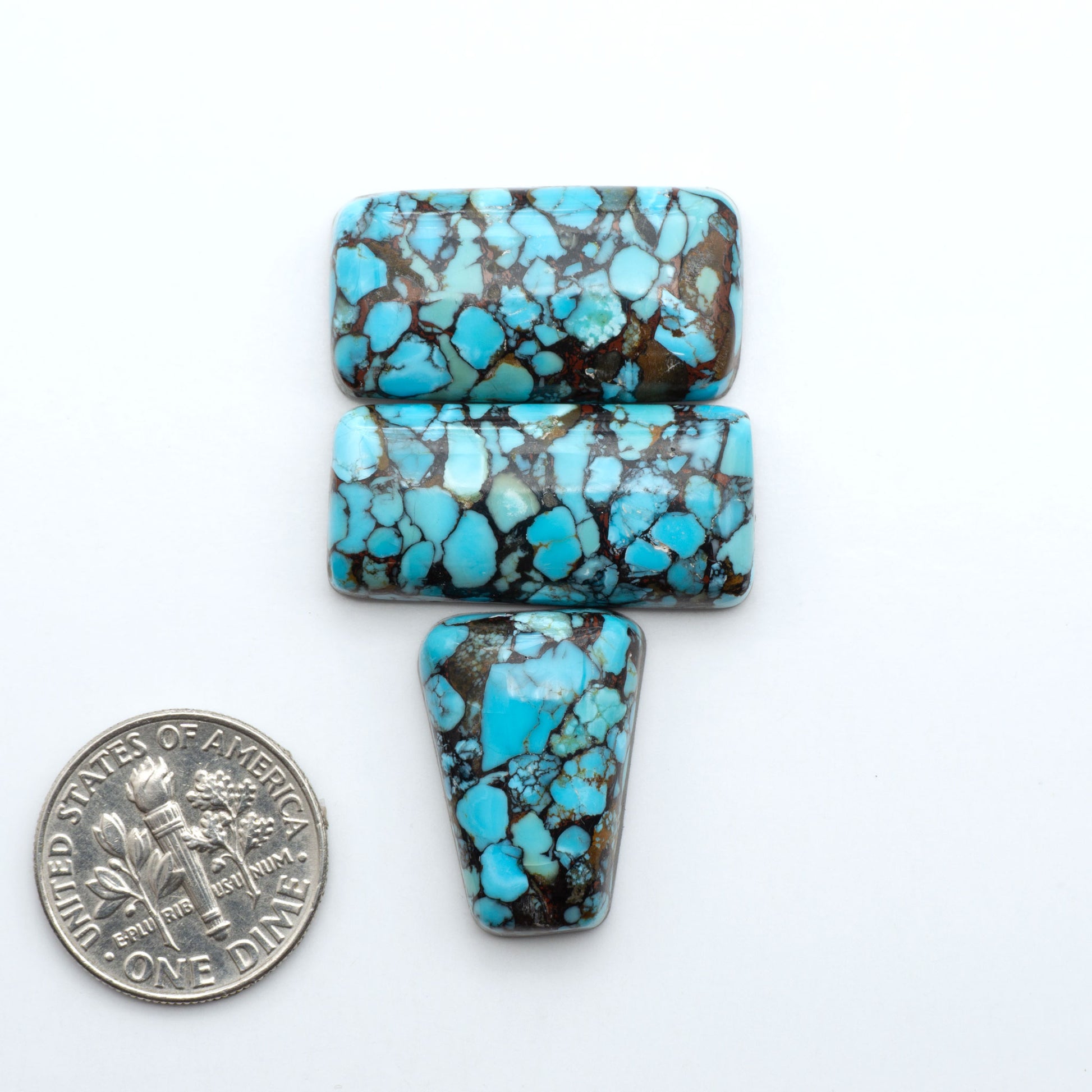 Pressed Turquoise nugget cabochons, composite material with a blue color and dark matrix on a white background, with a US dime for scale.