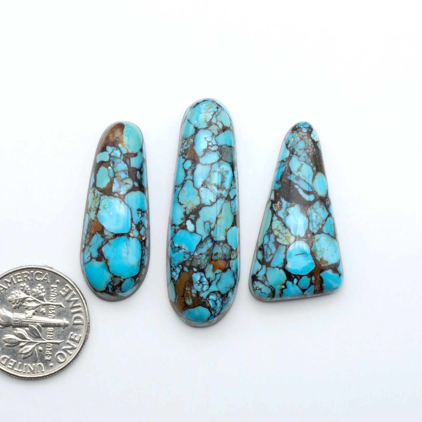 Pressed Turquoise nugget cabochons, composite material with a blue color and dark matrix on a white background, with a US dime for scale.