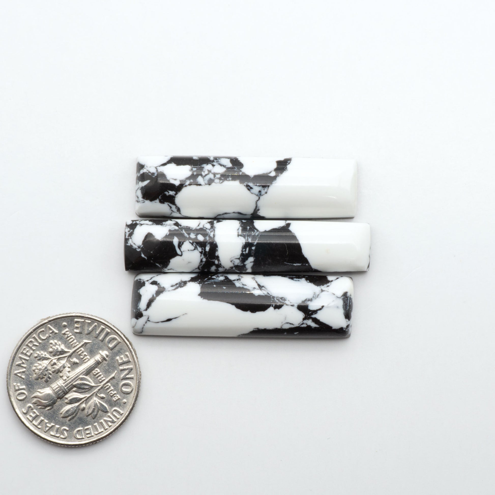White Buffalo composite cabochons, black and white gemstones on a white background with a US dime for scale