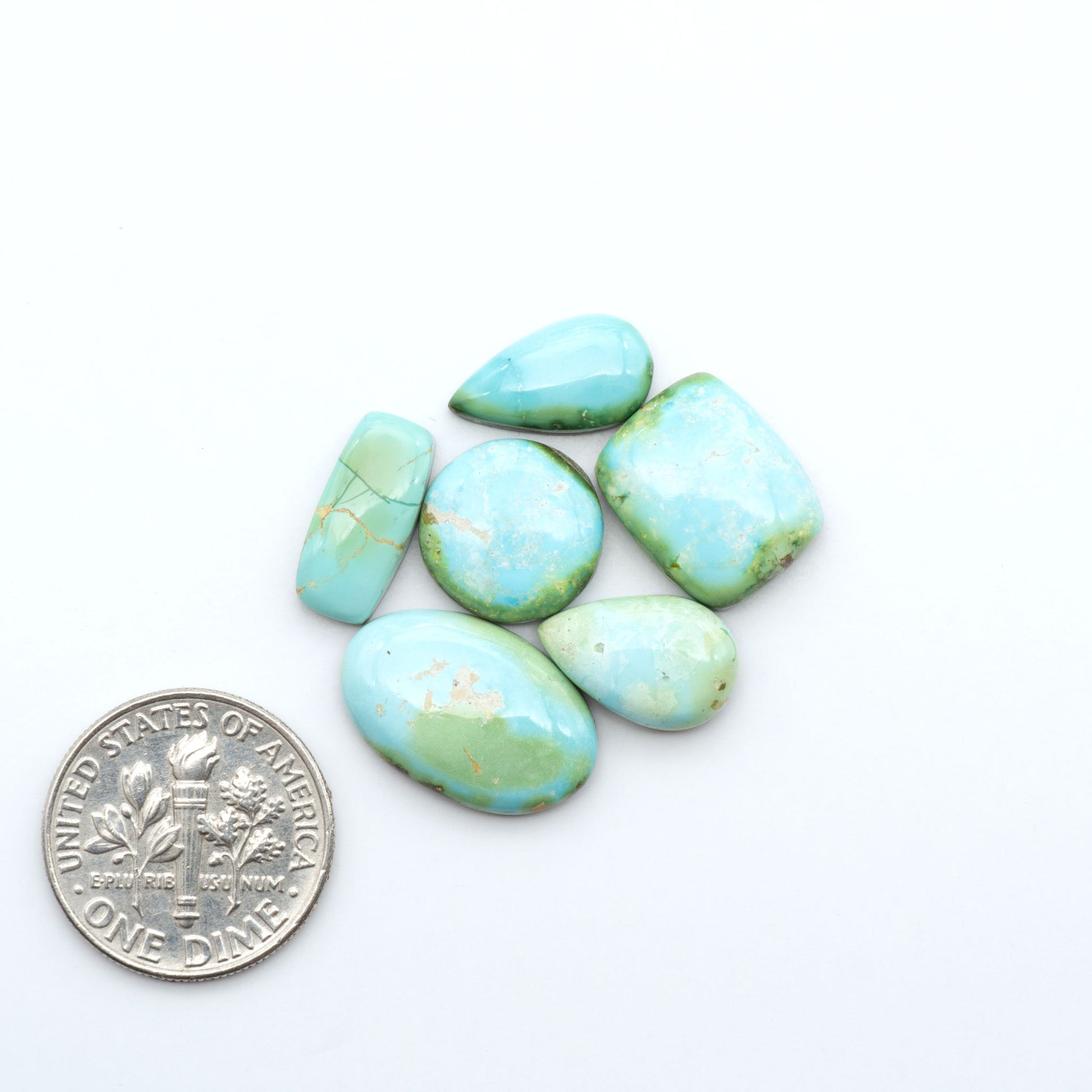 Sonoran Mountain Turquoise cabochons, blue-green color with natural matrix, polished stones on a white background, with a US dime for scale
