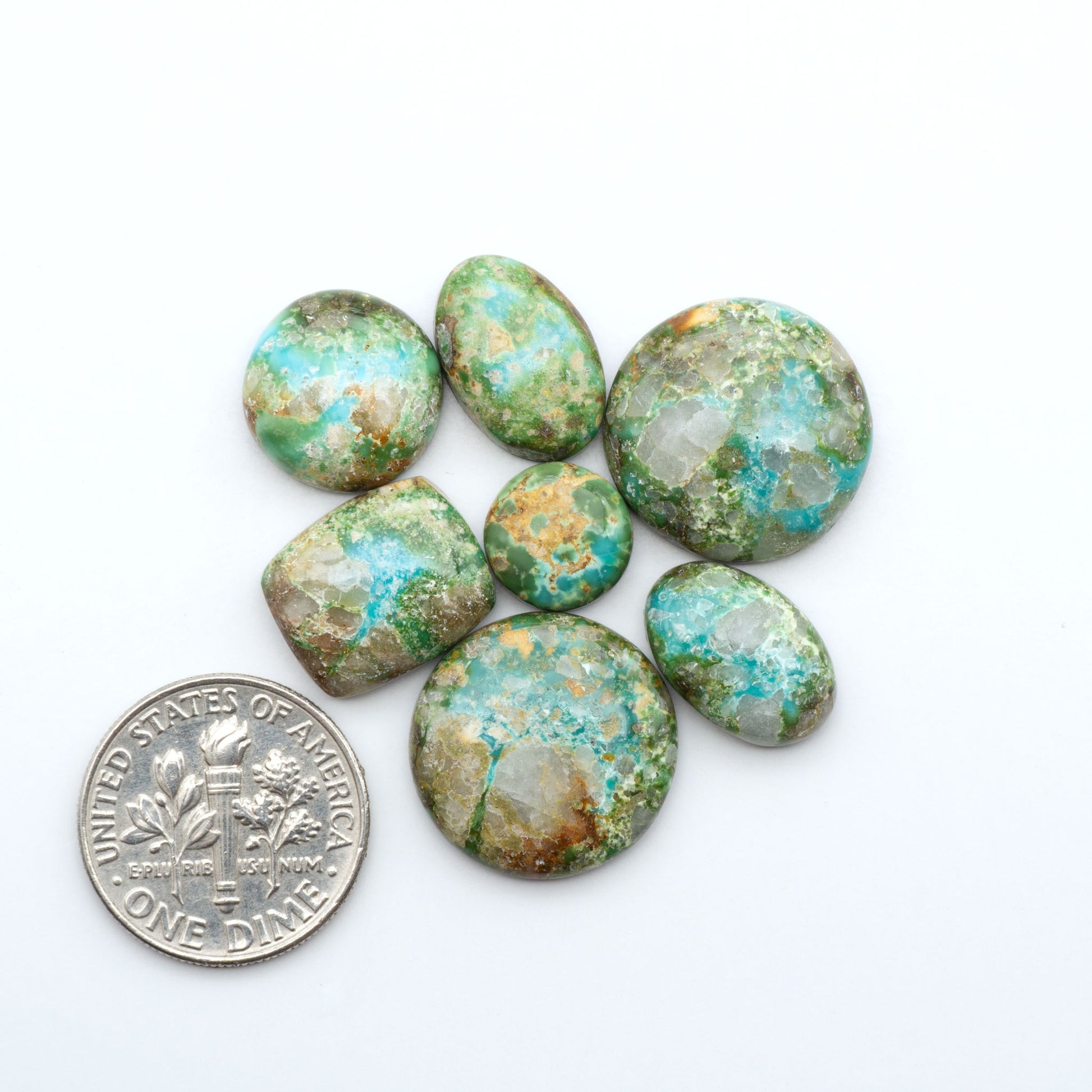 Sonoran Mountain Turquoise cabochons, blue-green color with natural matrix, polished stones on a white background, with a US dime for scale