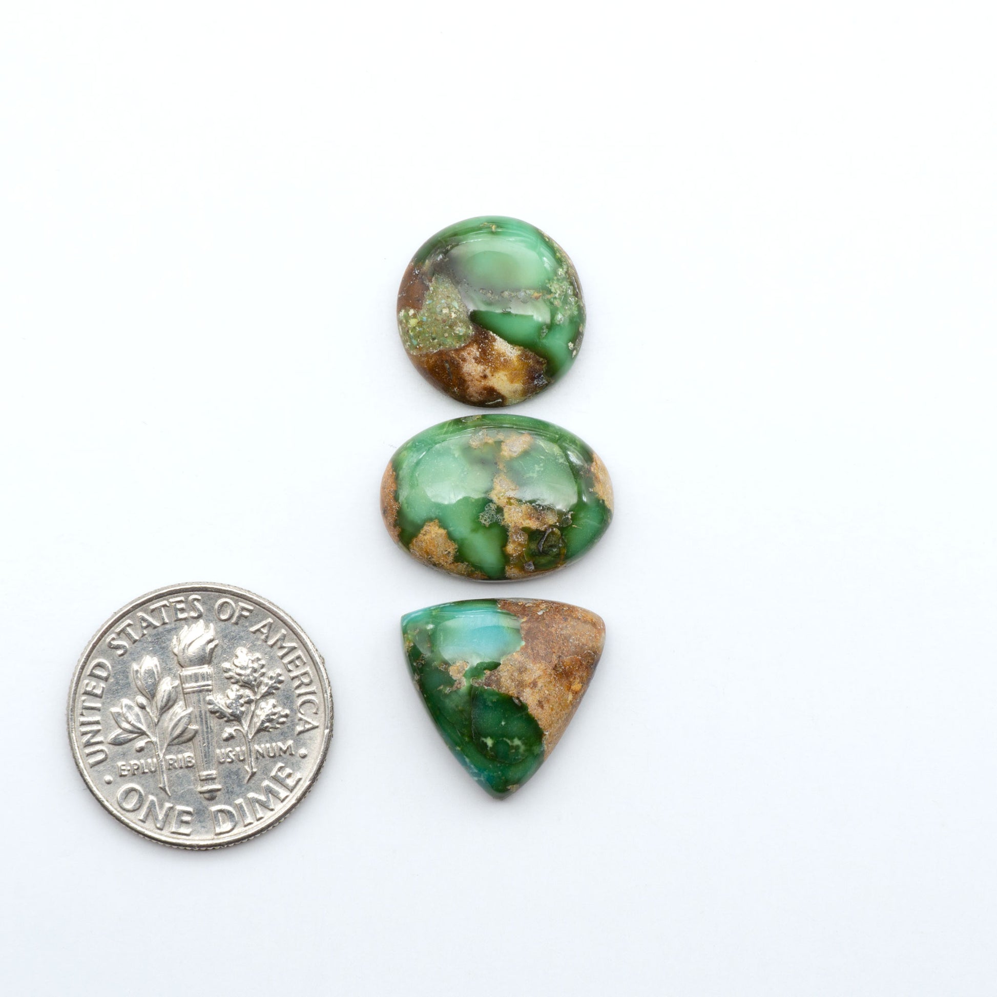 Sonoran Mountain Turquoise cabochons, blue-green color with natural matrix, polished stones on a white background, with a US dime for scale