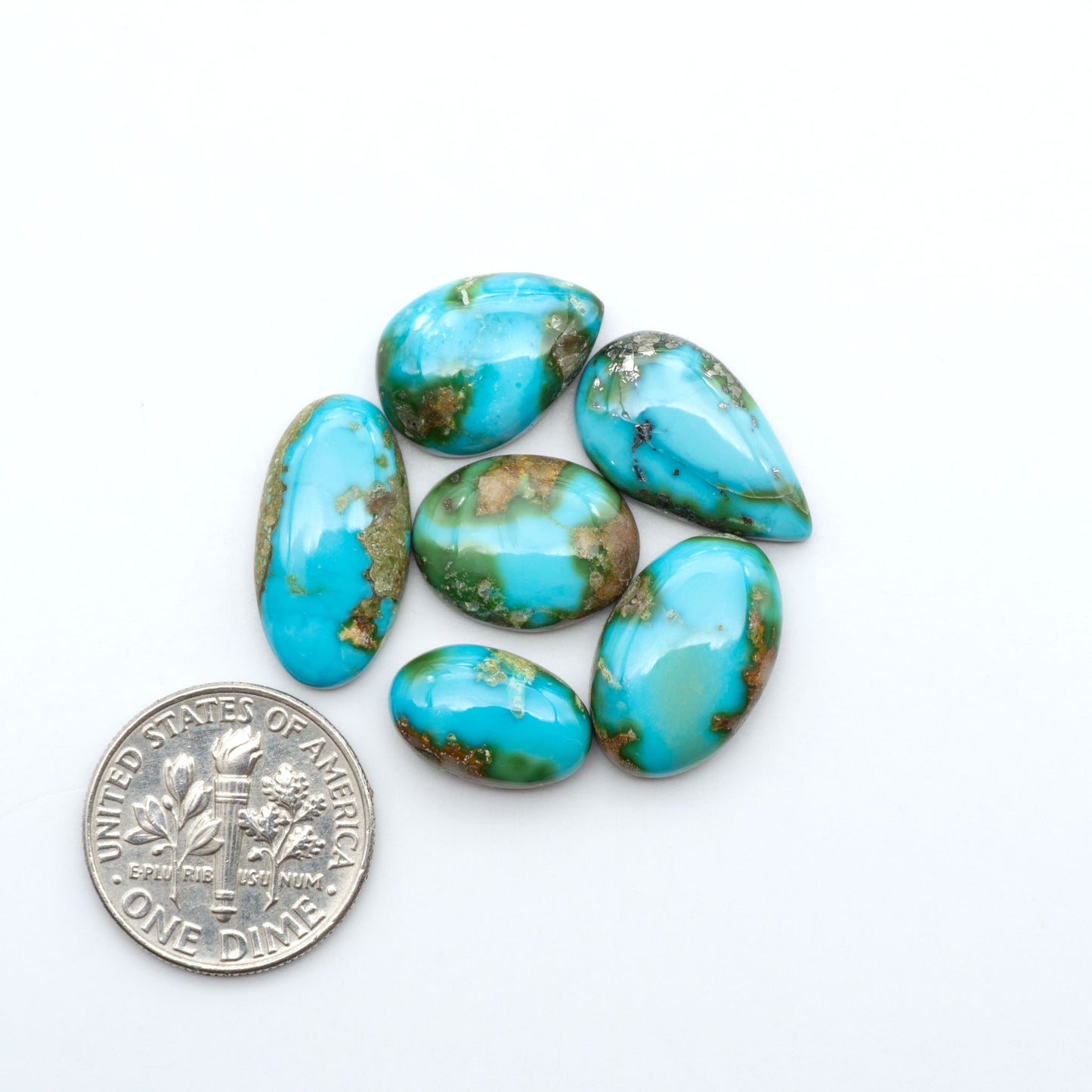 Sonoran Mountain Turquoise cabochons, blue-green color with natural matrix, polished stones on a white background, with a US dime for scale