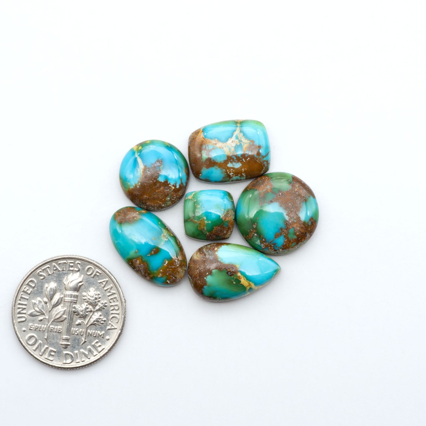 Sonoran Mountain Turquoise cabochons, blue-green color with natural matrix, polished stones on a white background, with a US dime for scale