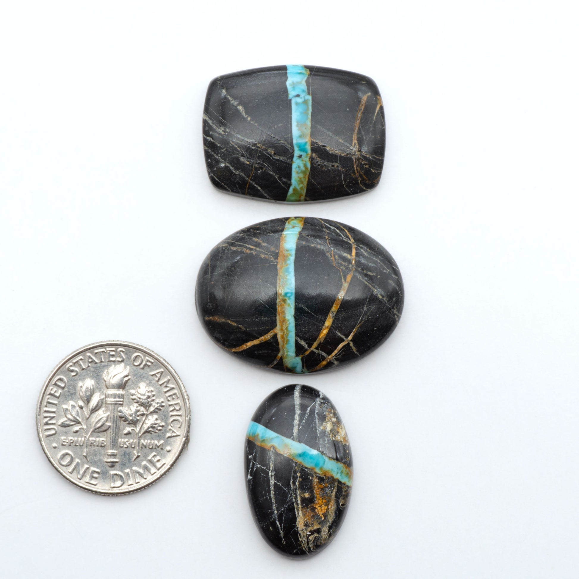 Black Jack turquoise cabochons, blue-green color with black matrix, polished stones on a white background with a US dime for scale