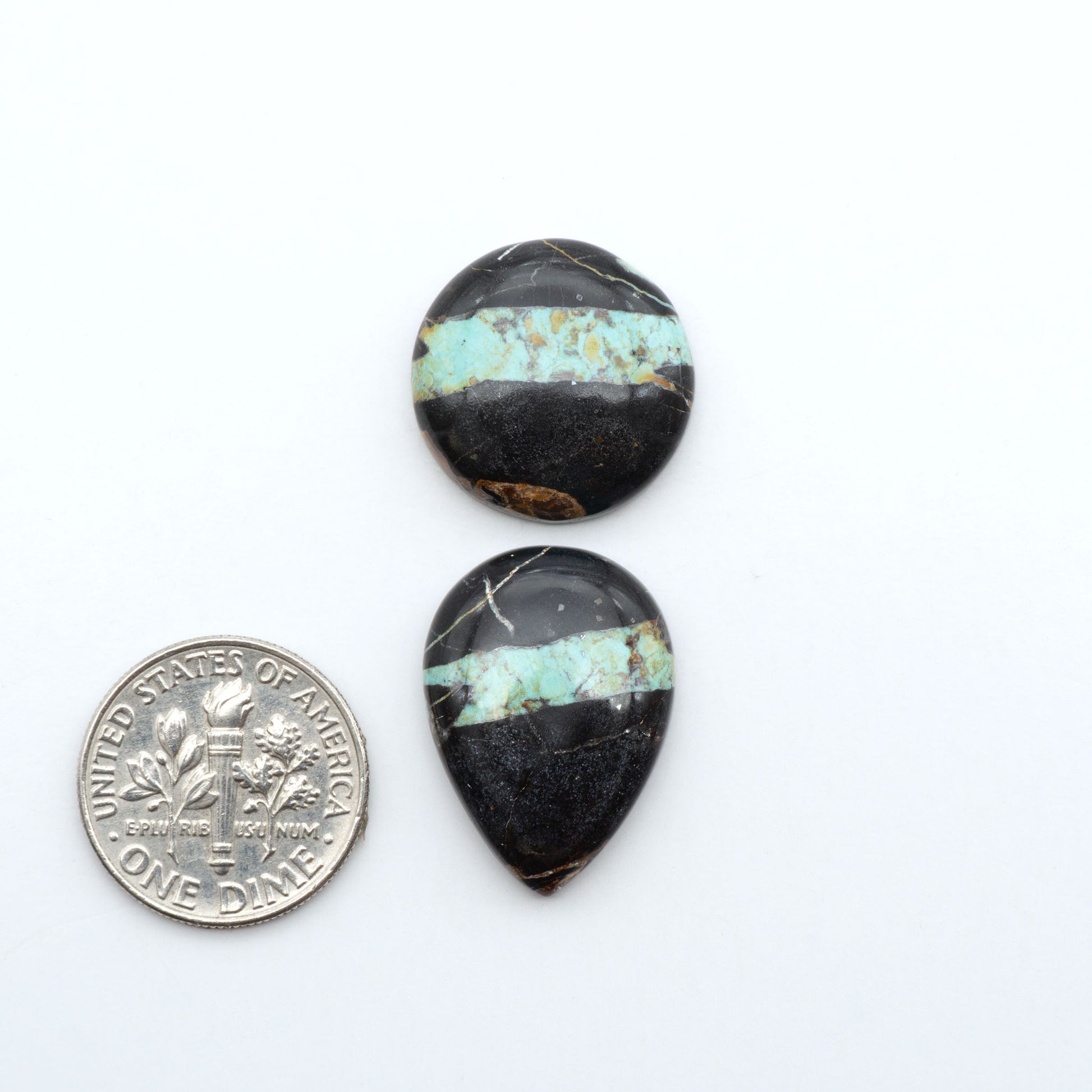 Black Jack turquoise cabochons, blue-green color with black matrix, polished stones on a white background with a US dime for scale