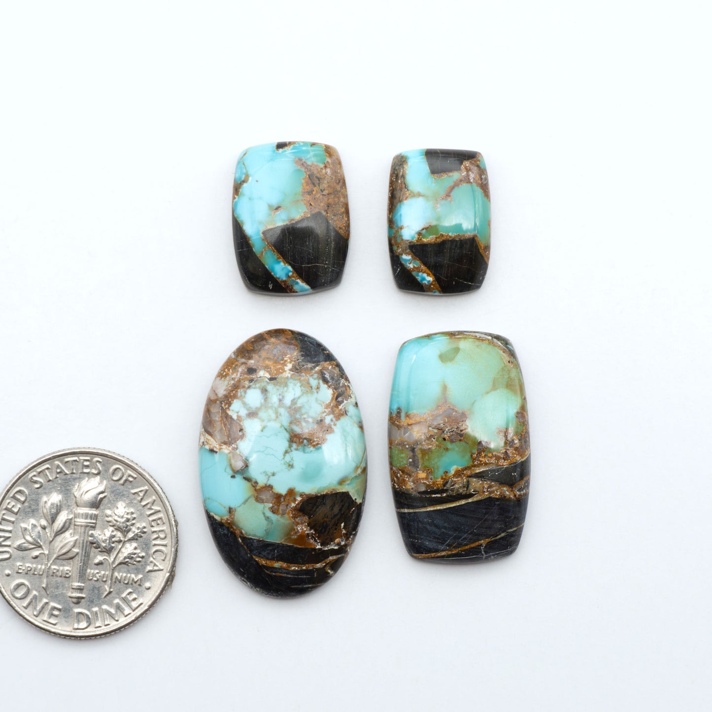 Black Jack turquoise cabochons, blue-green color with black matrix, polished stones on a white background with a US dime for scale