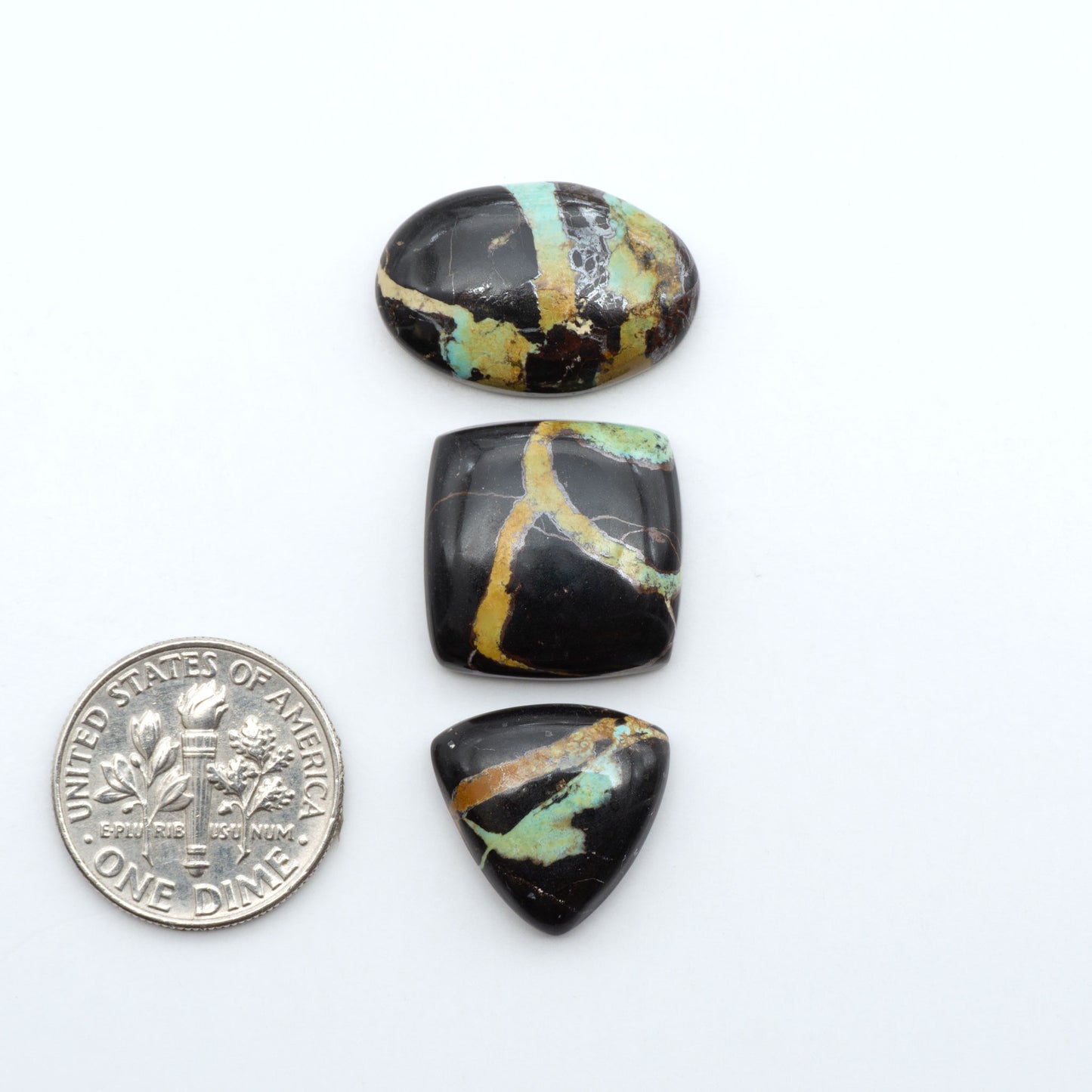 Black Jack turquoise cabochons, blue-green color with black matrix, polished stones on a white background with a US dime for scale