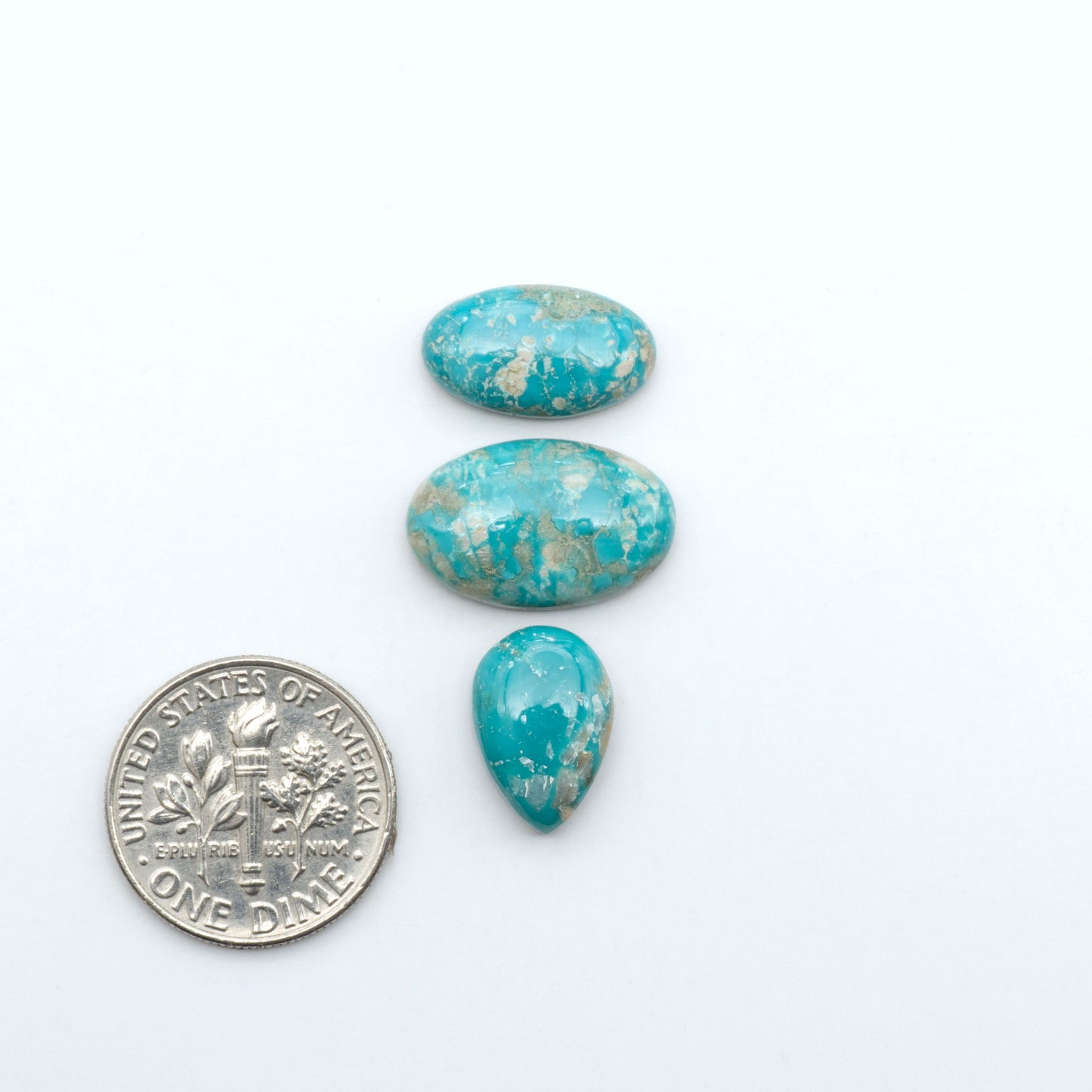 Fox Turquoise cabochons, polished gemstones with natural matrix on a white background, with a US dime for scale