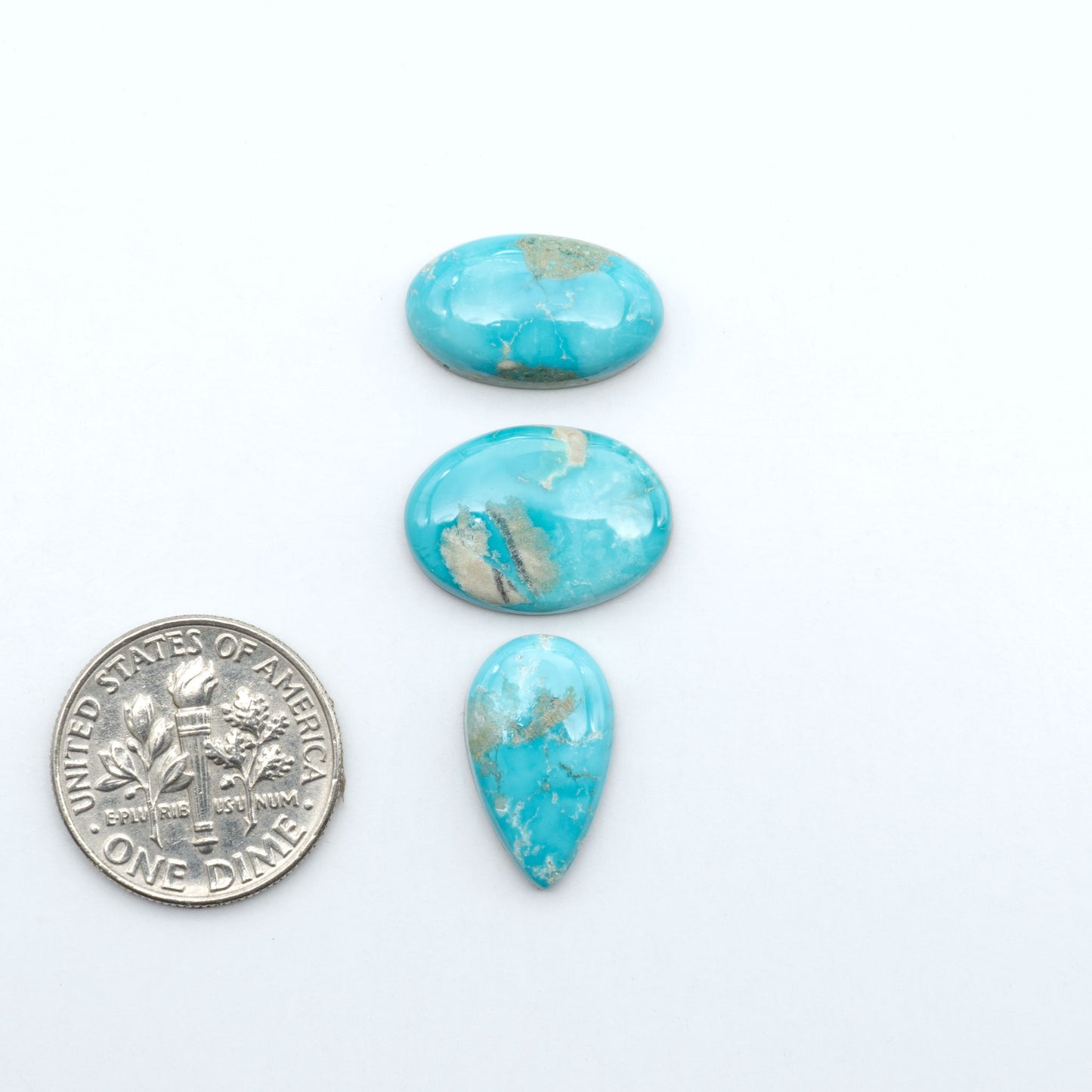 Fox Turquoise cabochons, polished gemstones with natural matrix on a white background, with a US dime for scale
