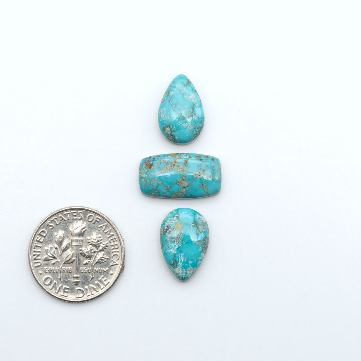Fox Turquoise cabochons, polished gemstones with natural matrix on a white background, with a US dime for scale