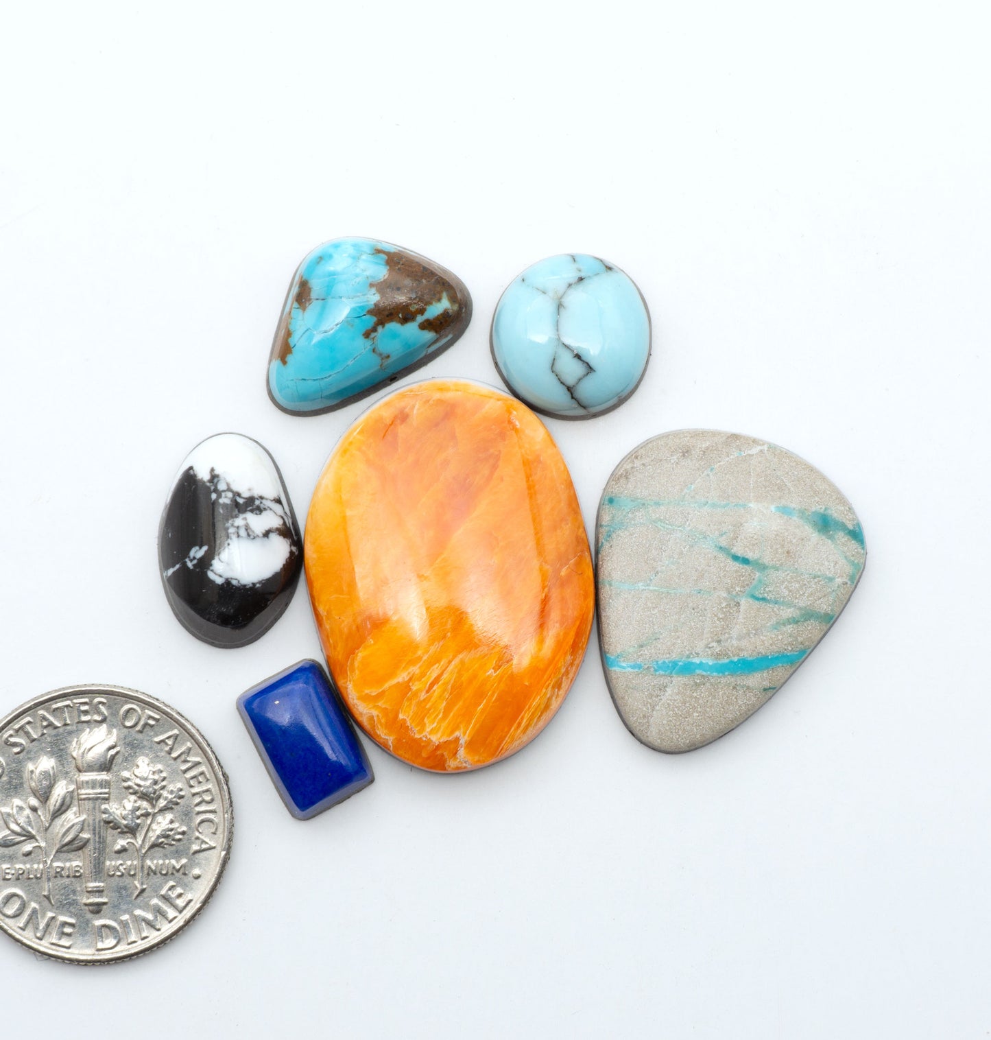 Mixed gemstone cabochons with assorted colors, patterns, and materials on a white background with a US dime for scale
