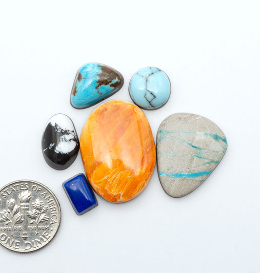 Mixed gemstone cabochons with assorted colors, patterns, and materials on a white background with a US dime for scale