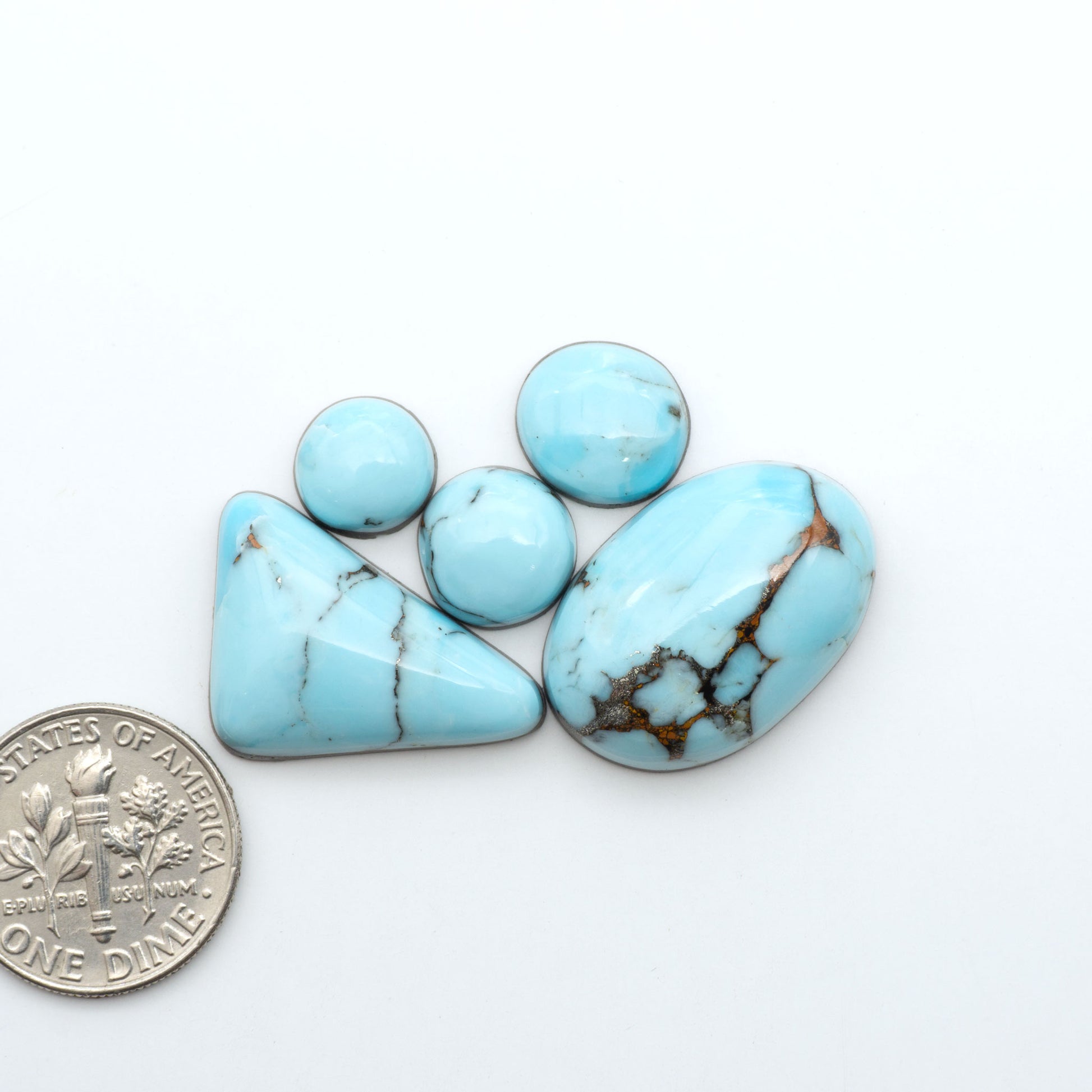 Pressed Turquoise nugget cabochons, composite material with a blue color and dark matrix on a white background, with a US dime for scale.