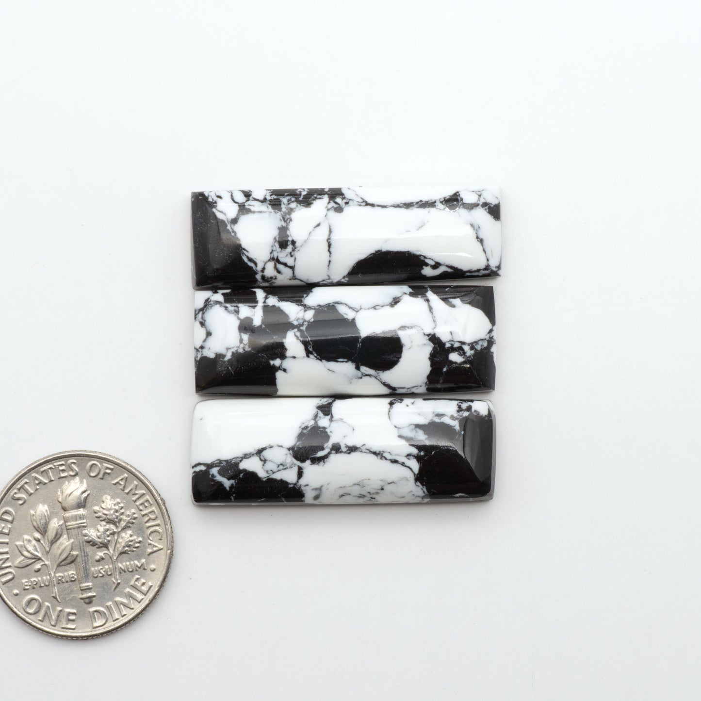 White Buffalo composite cabochons, black and white gemstones on a white background with a US dime for scale