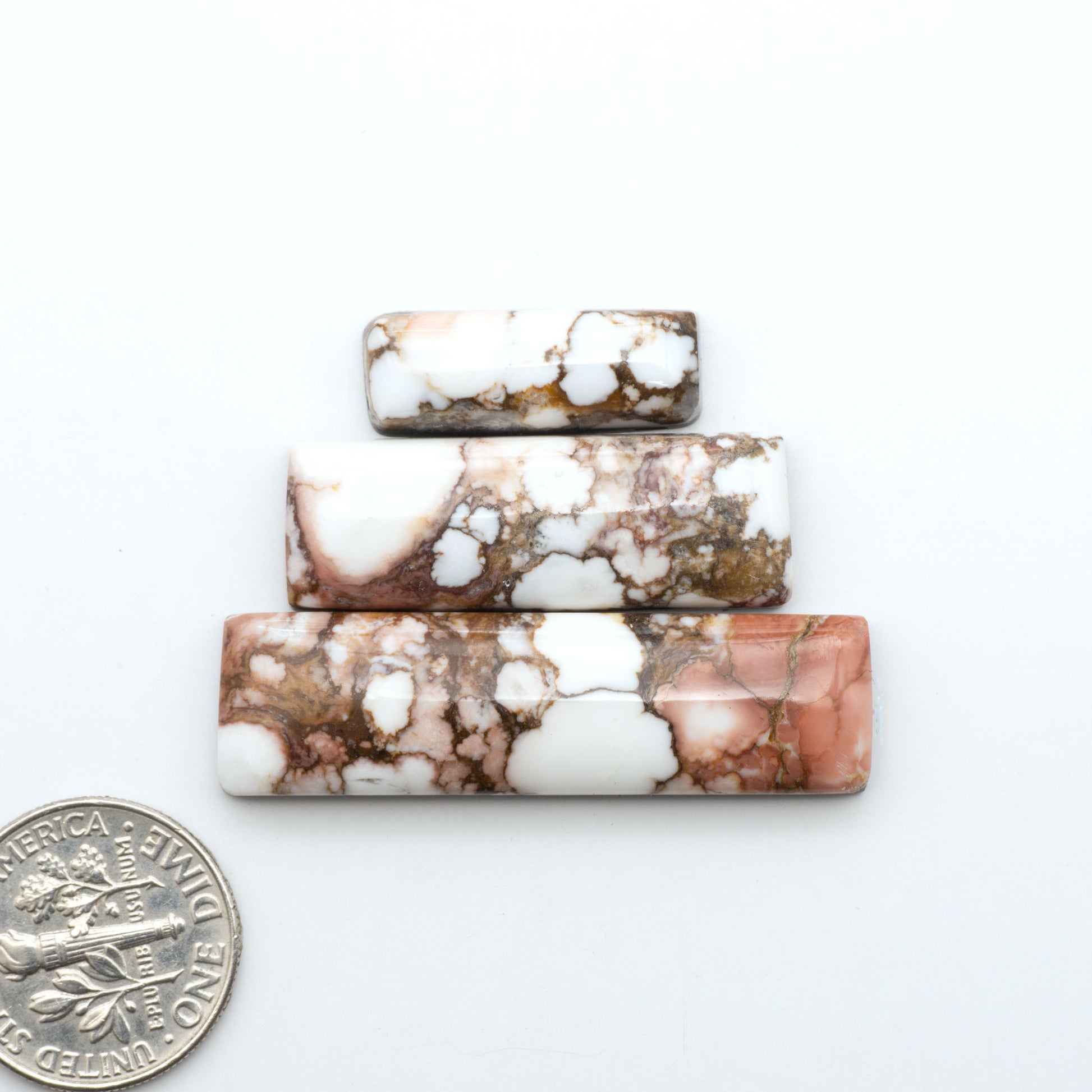 Wild Horse Magnesite cabochons, white gemstones with brown matrix on a white background, with a US dime for scale