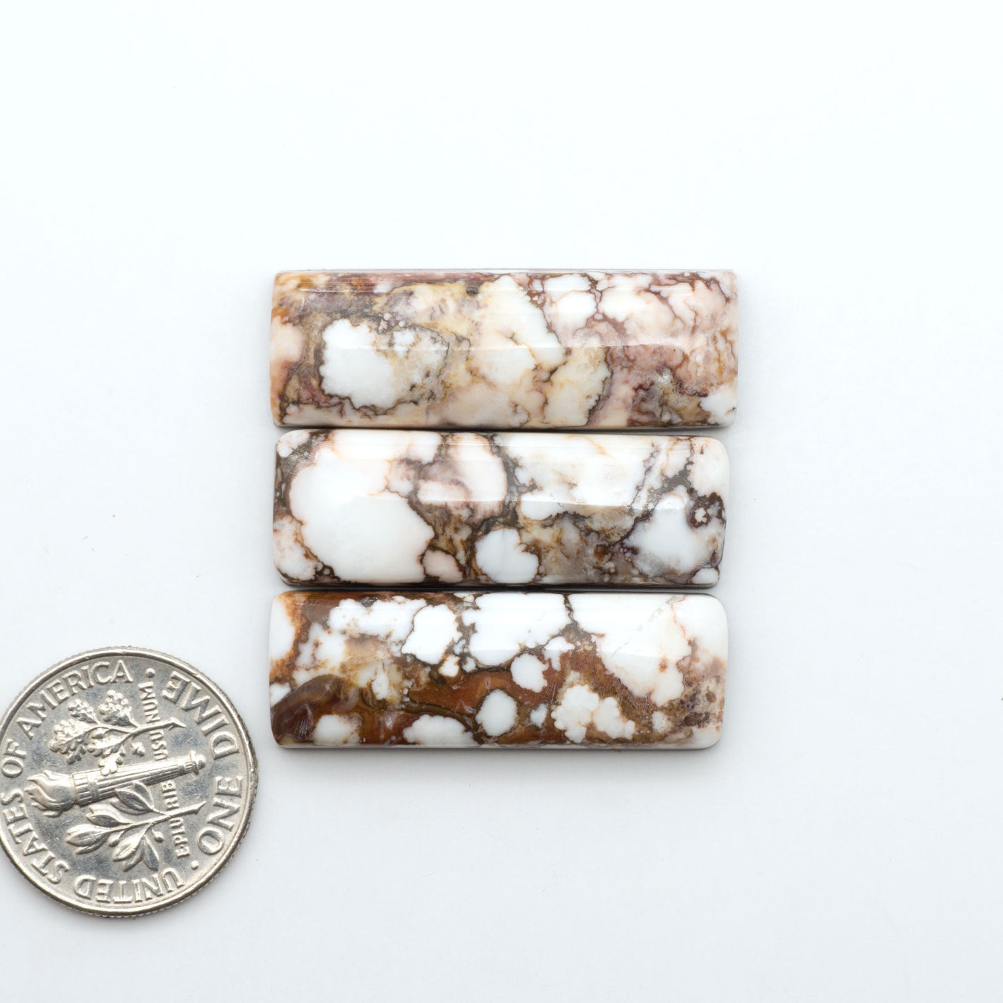 Wild Horse Magnesite cabochons, white gemstones with brown matrix on a white background, with a US dime for scale