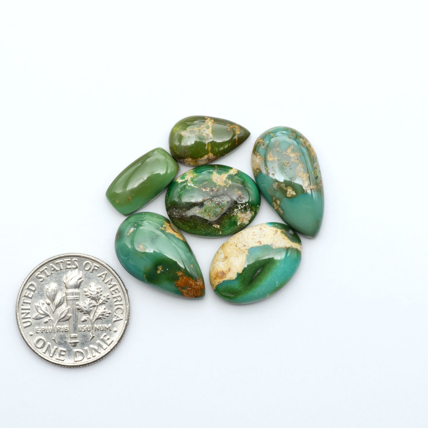 Sonoran Mountain Turquoise cabochons, blue-green color with natural matrix, polished stones on a white background, with a US dime for scale