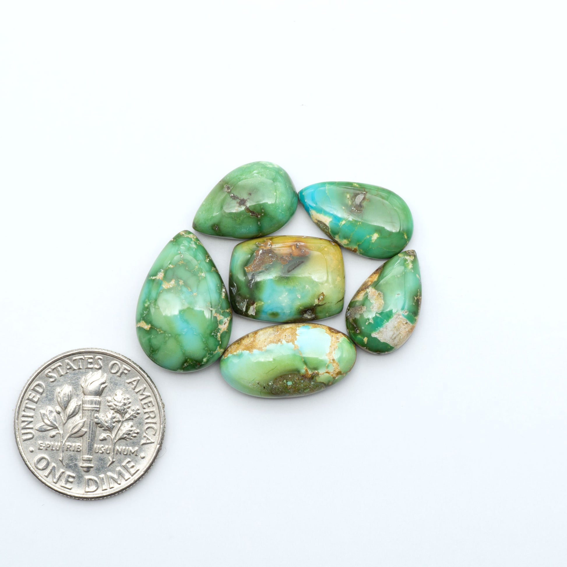 Sonoran Mountain Turquoise cabochons, blue-green color with natural matrix, polished stones on a white background, with a US dime for scale