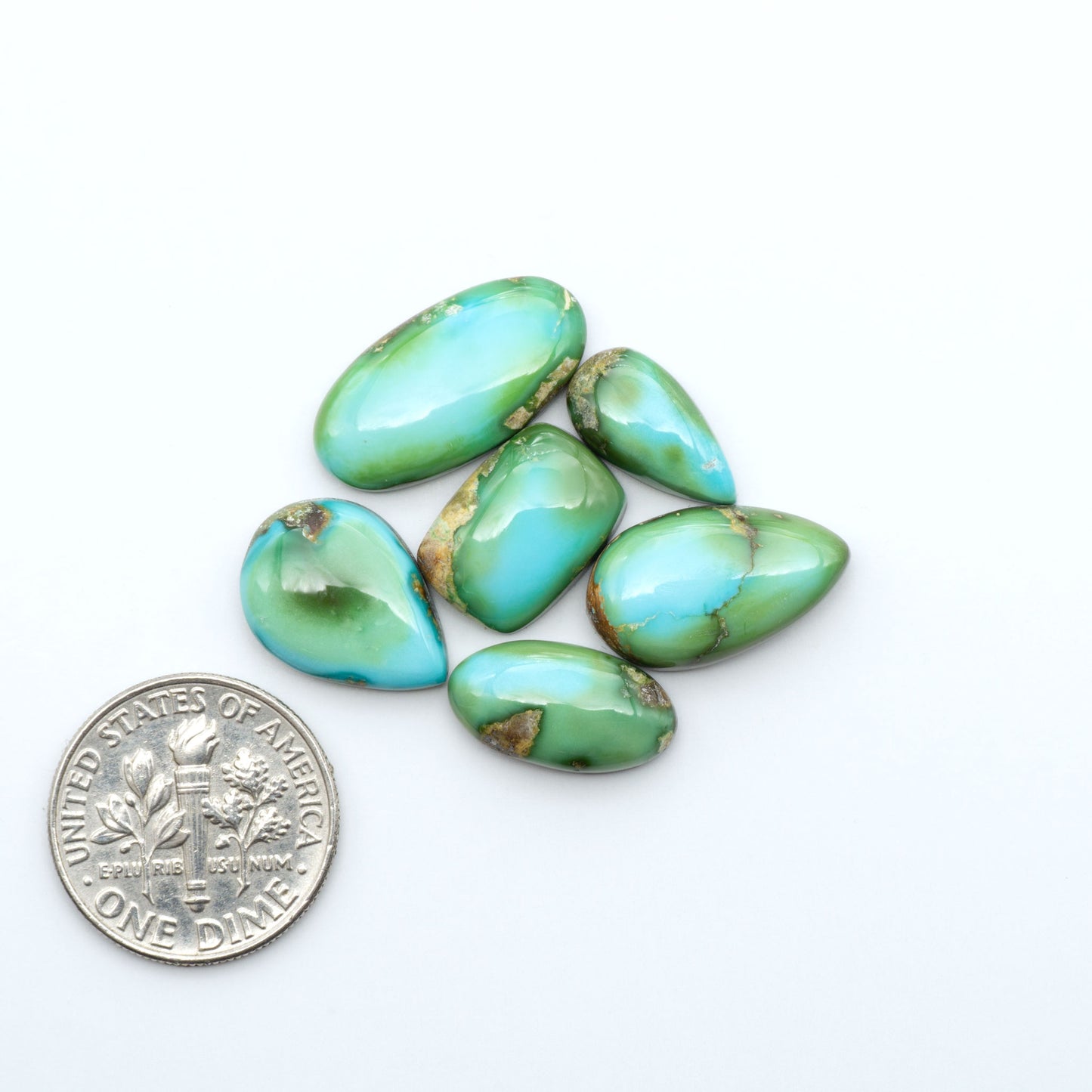 Sonoran Mountain Turquoise cabochons, blue-green color with natural matrix, polished stones on a white background, with a US dime for scale