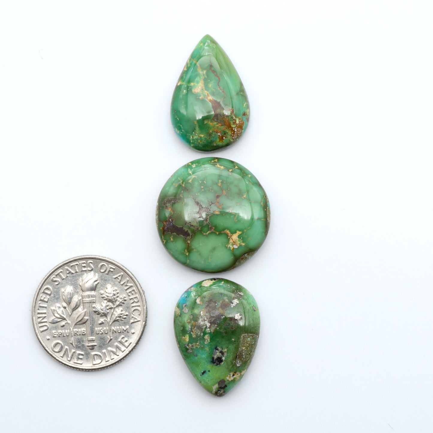 Sonoran Mountain Turquoise cabochons, blue-green color with natural matrix, polished stones on a white background, with a US dime for scale