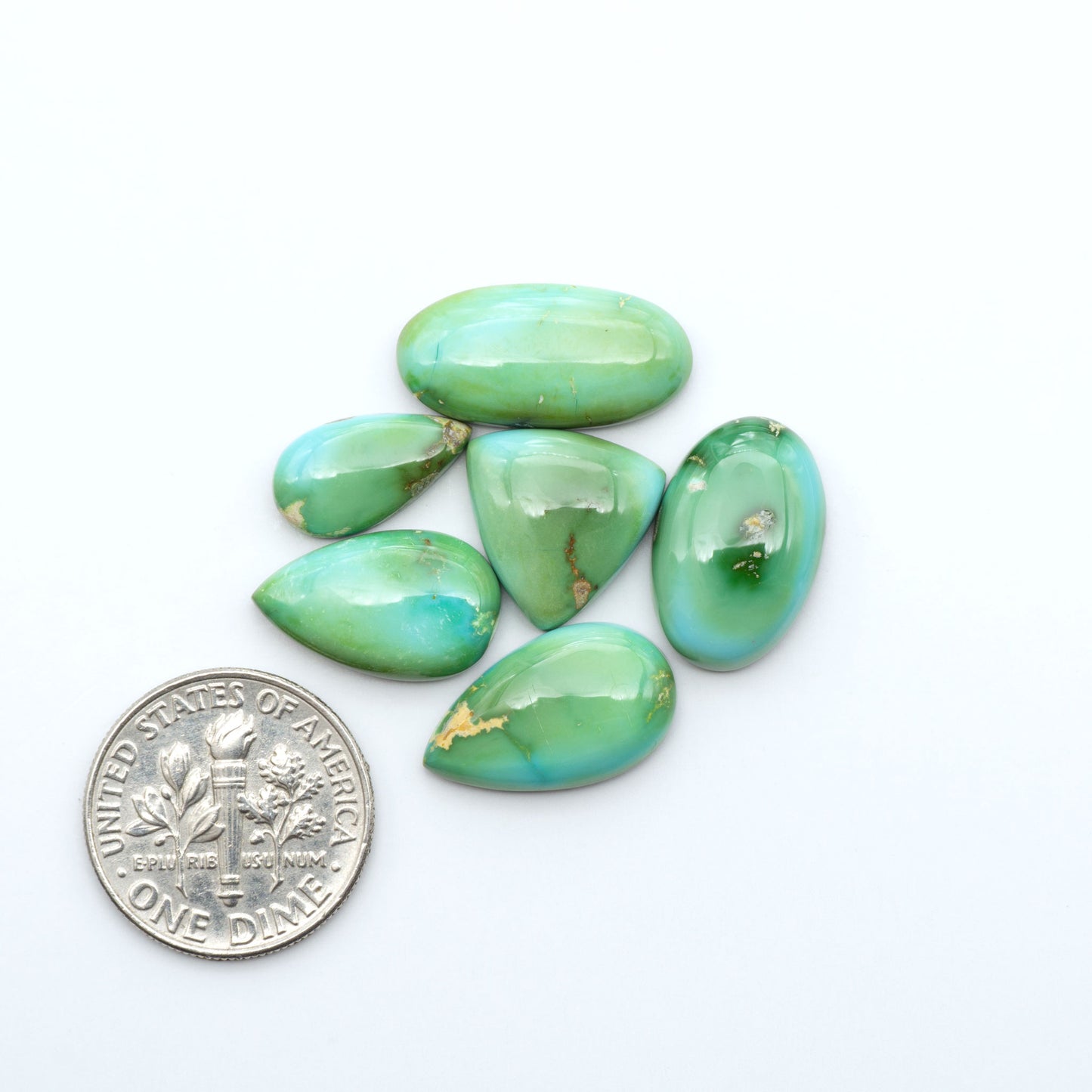 Sonoran Mountain Turquoise cabochons, blue-green color with natural matrix, polished stones on a white background, with a US dime for scale