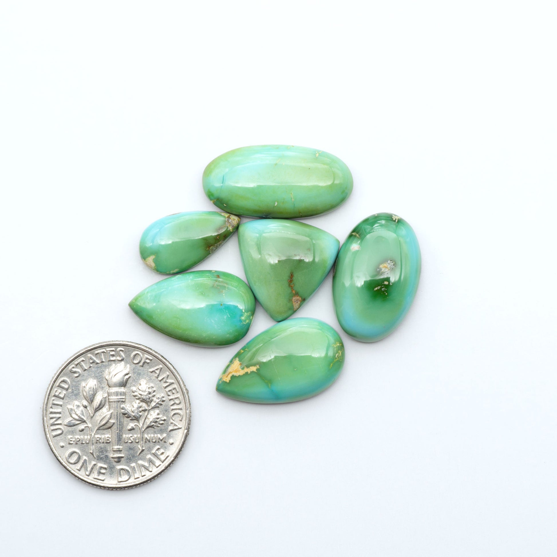 Sonoran Mountain Turquoise cabochons, blue-green color with natural matrix, polished stones on a white background, with a US dime for scale