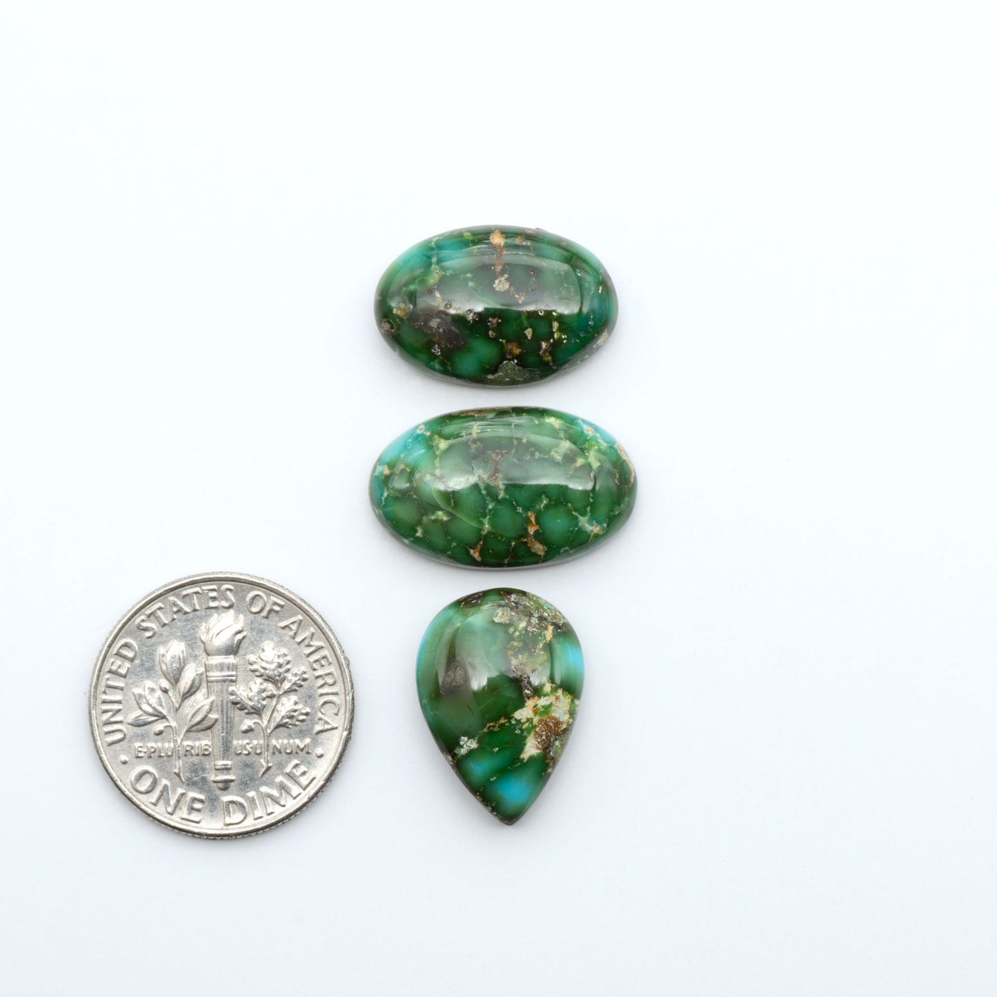 Sonoran Mountain Turquoise cabochons, blue-green color with natural matrix, polished stones on a white background, with a US dime for scale