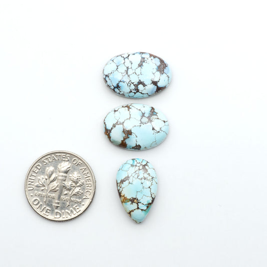 Golden Hills Turquoise cabochons, icy blue to lavender tones with chocolate matrix, polished stones on a white background with a US dime for scale