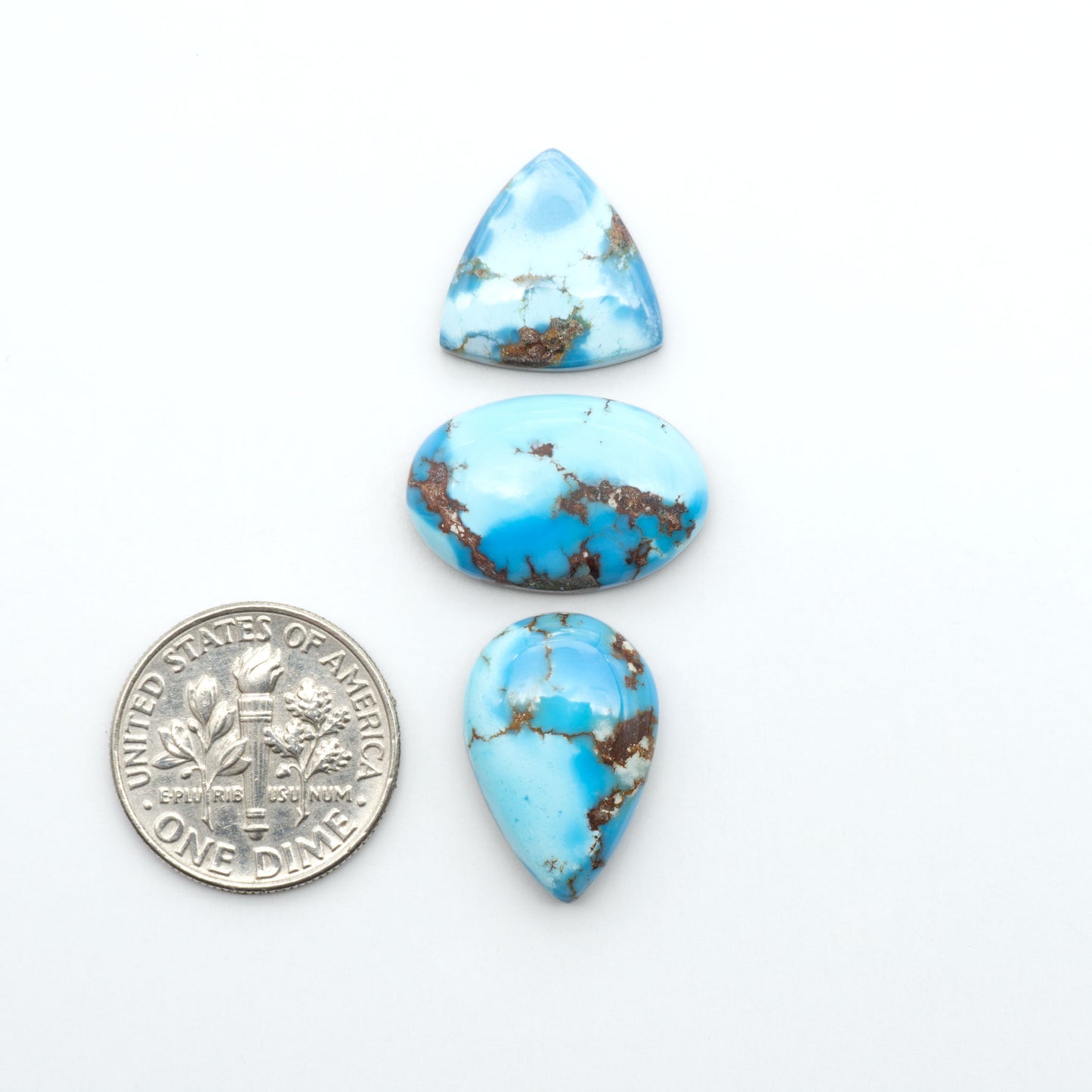Golden Hills Turquoise cabochons, icy blue to lavender tones with chocolate matrix, polished stones on a white background with a US dime for scale