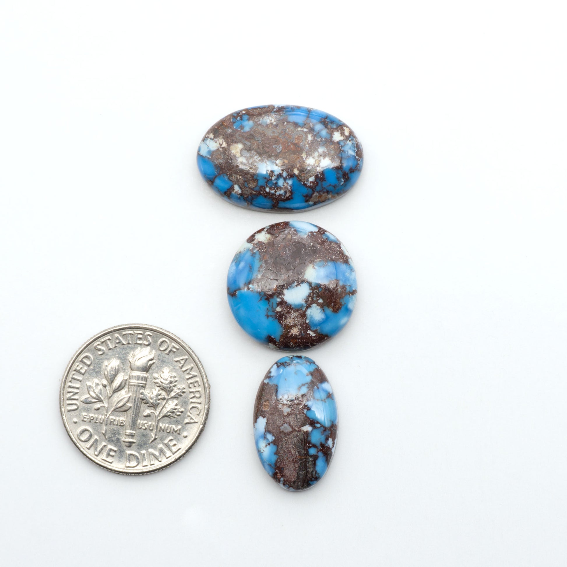 Golden Hills Turquoise cabochons, icy blue to lavender tones with chocolate matrix, polished stones on a white background with a US dime for scale
