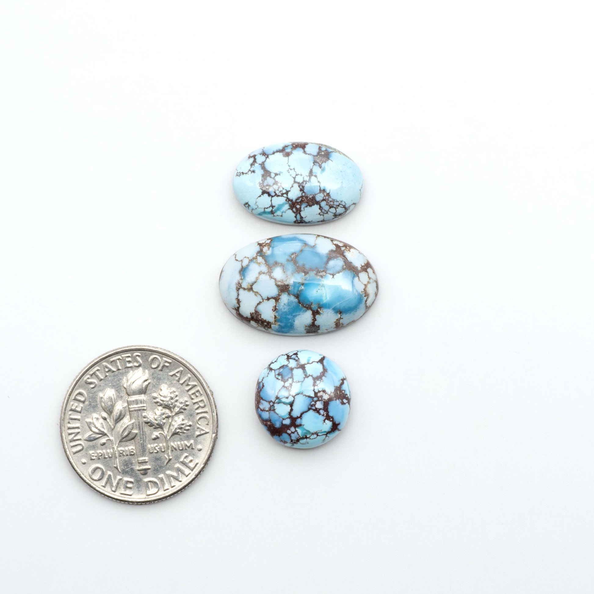 Golden Hills Turquoise cabochons, icy blue to lavender tones with chocolate matrix, polished stones on a white background with a US dime for scale