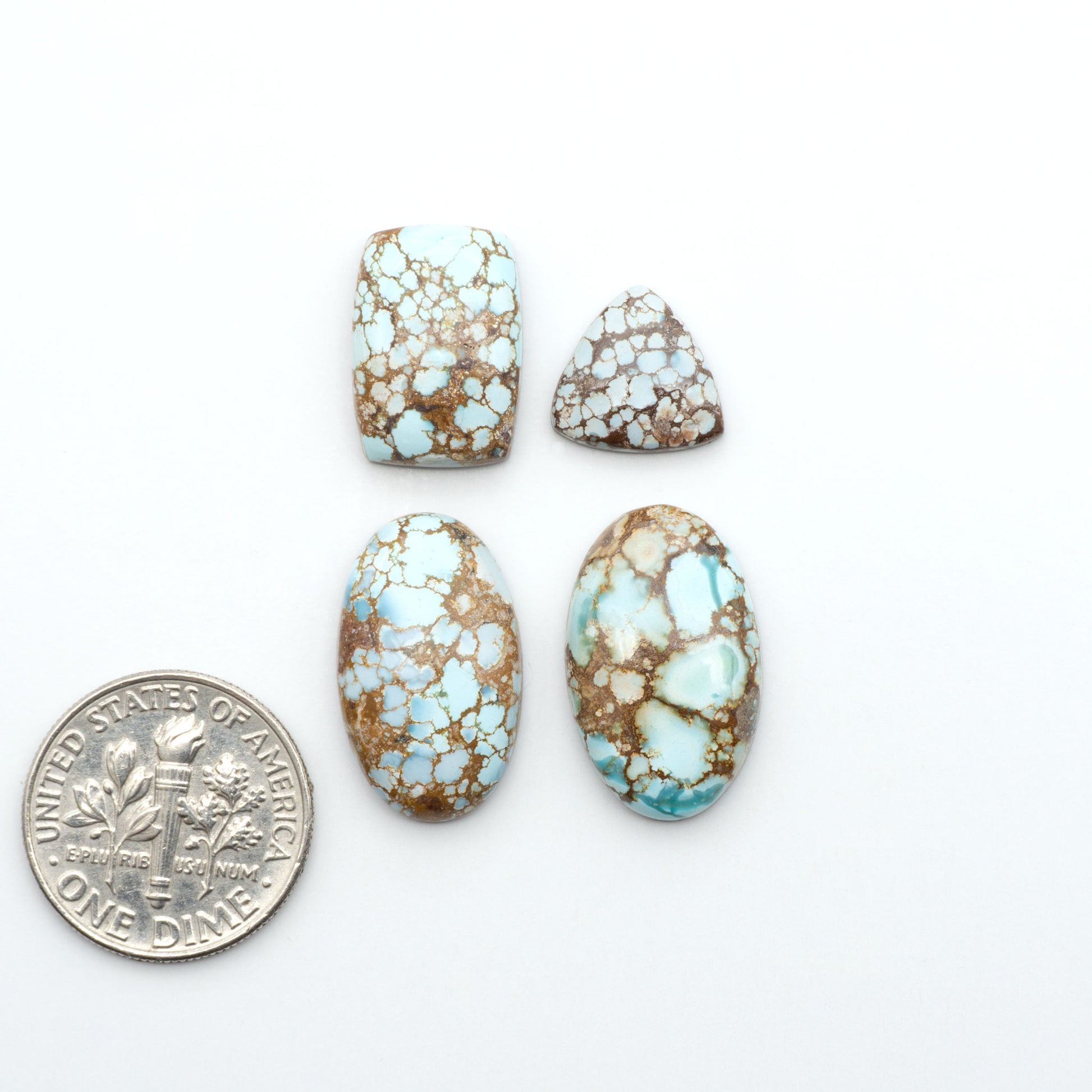 Golden Hills Turquoise cabochons, icy blue to lavender tones with chocolate matrix, polished stones on a white background with a US dime for scale