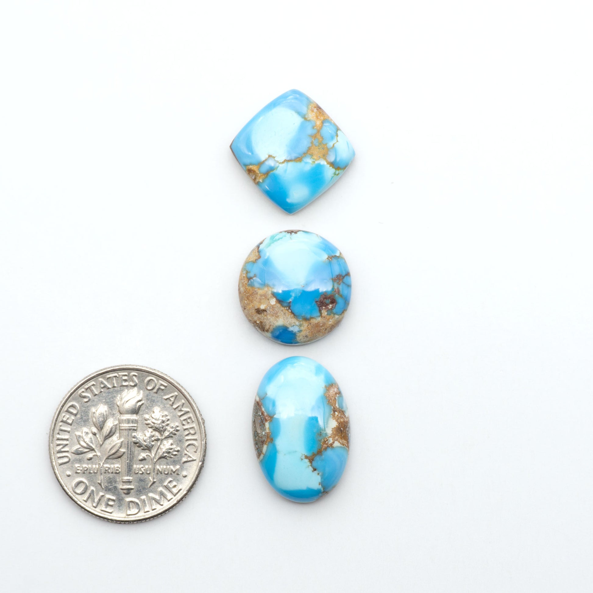 Golden Hills Turquoise cabochons, icy blue to lavender tones with chocolate matrix, polished stones on a white background with a US dime for scale