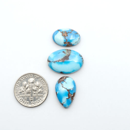 Golden Hills Turquoise cabochons, icy blue to lavender tones with chocolate matrix, polished stones on a white background with a US dime for scale