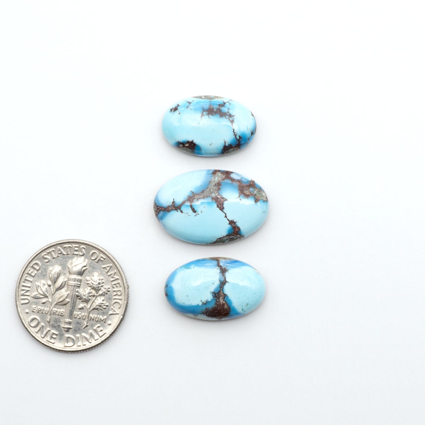 Golden Hills Turquoise cabochons, icy blue to lavender tones with chocolate matrix, polished stones on a white background with a US dime for scale