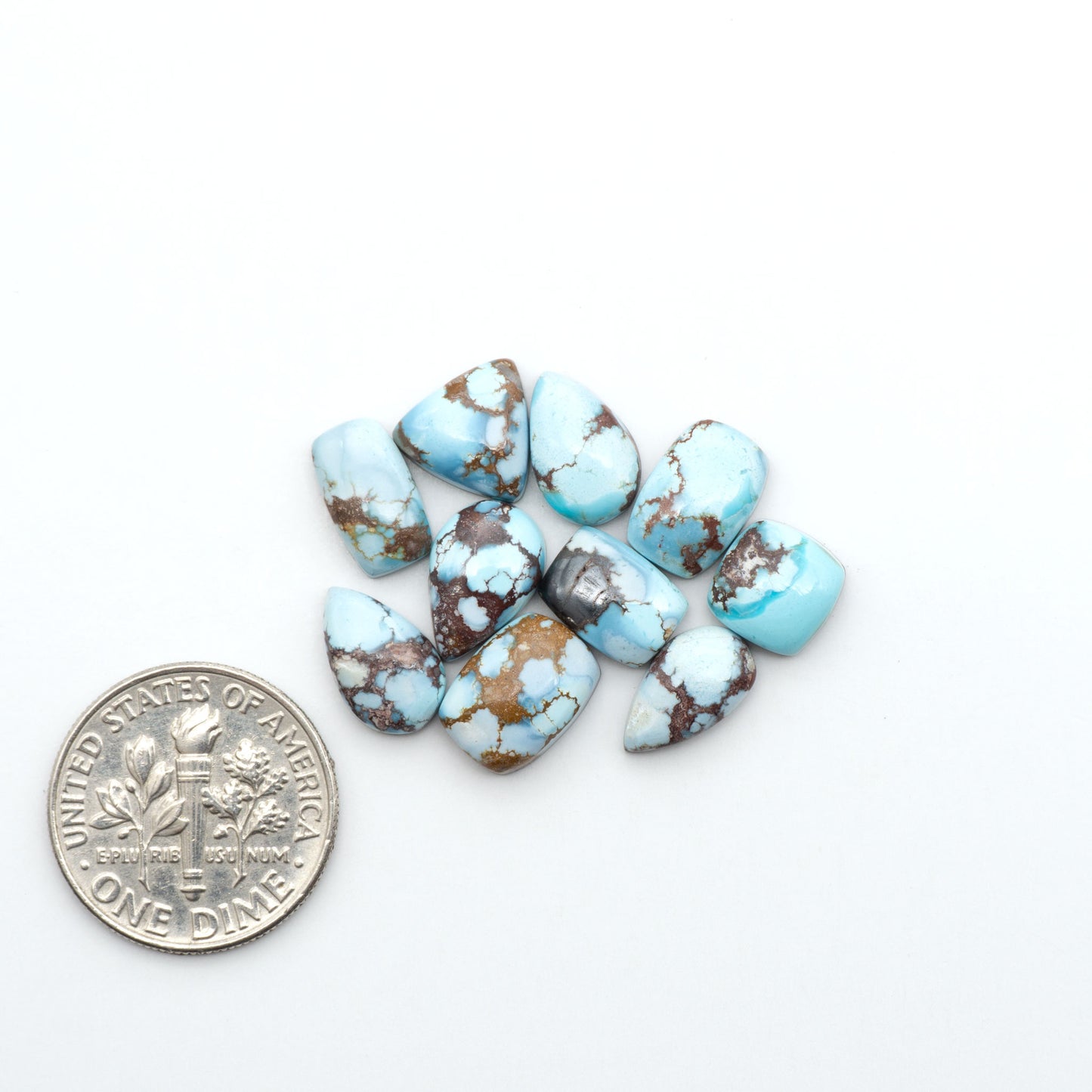 Golden Hills Turquoise cabochons, icy blue to lavender tones with chocolate matrix, polished stones on a white background with a US dime for scale