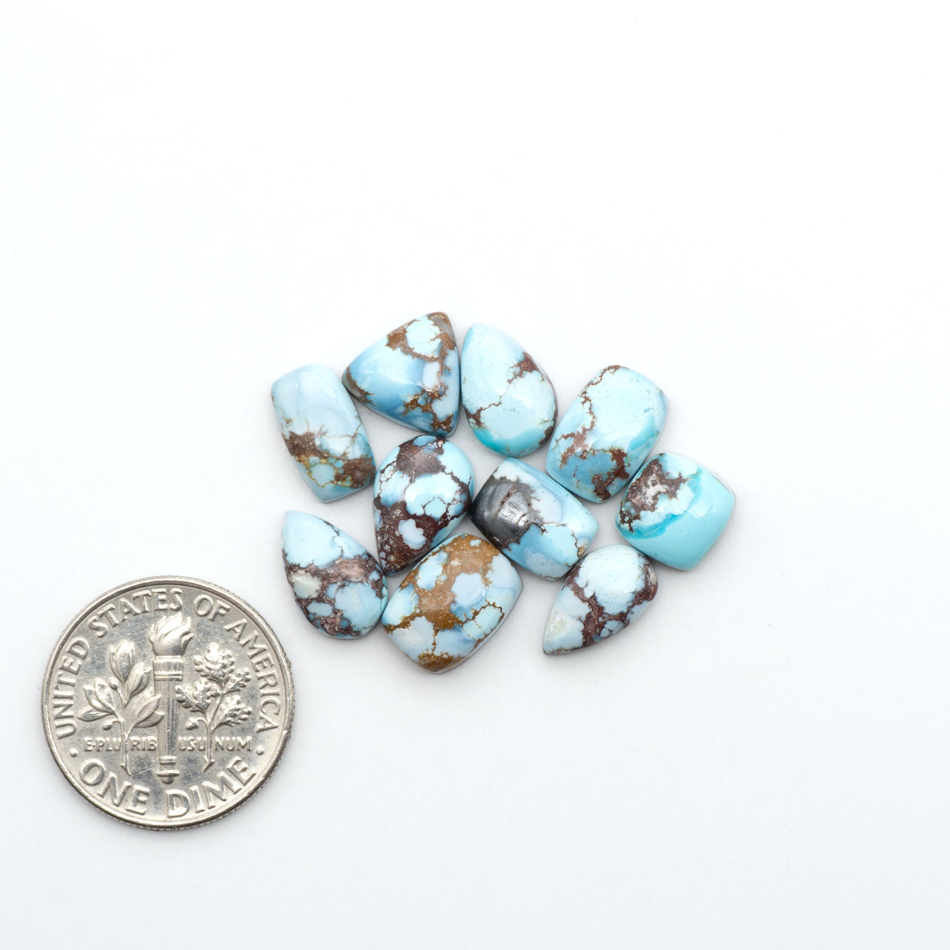 Golden Hills Turquoise cabochons, icy blue to lavender tones with chocolate matrix, polished stones on a white background with a US dime for scale