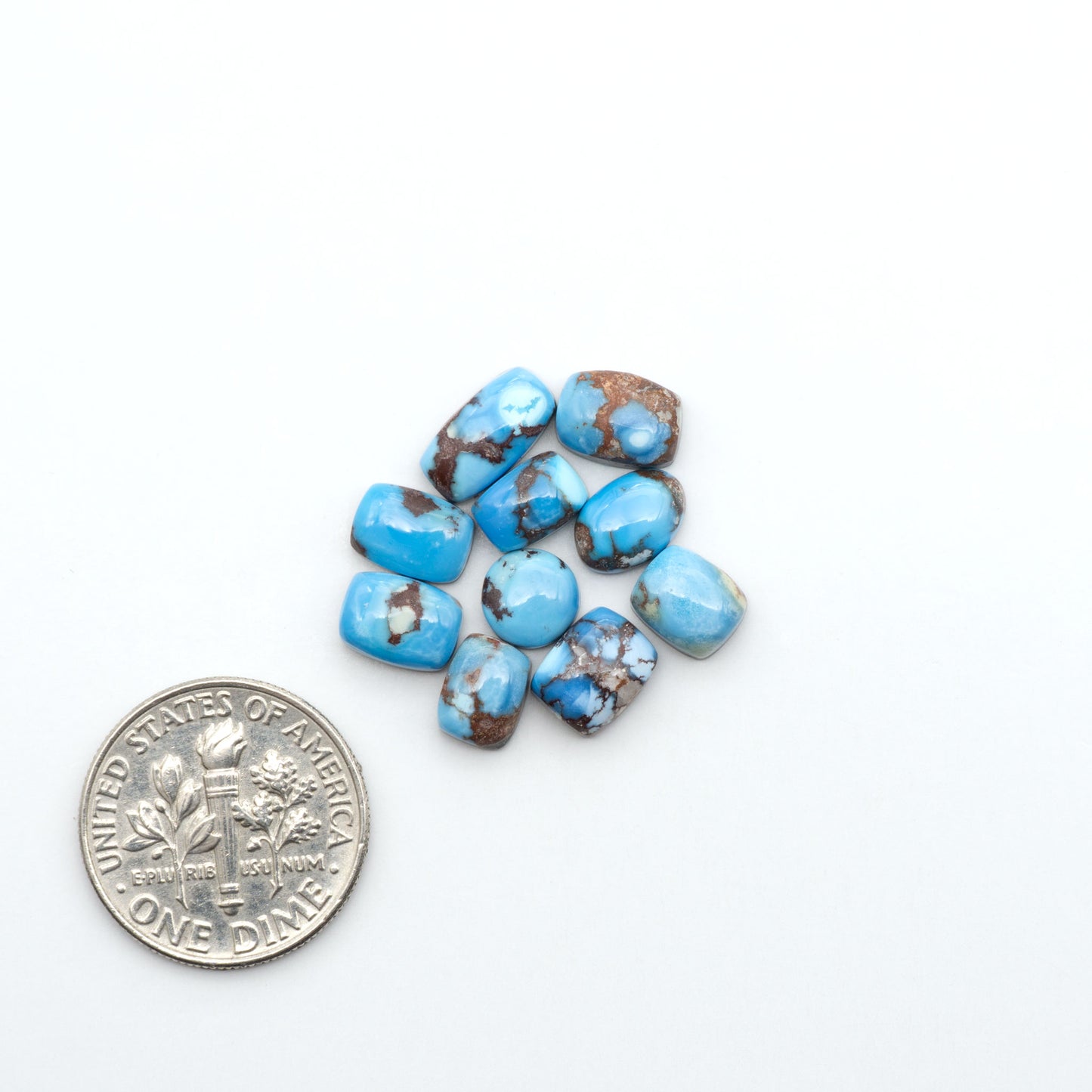 Golden Hills Turquoise cabochons, icy blue to lavender tones with chocolate matrix, polished stones on a white background with a US dime for scale