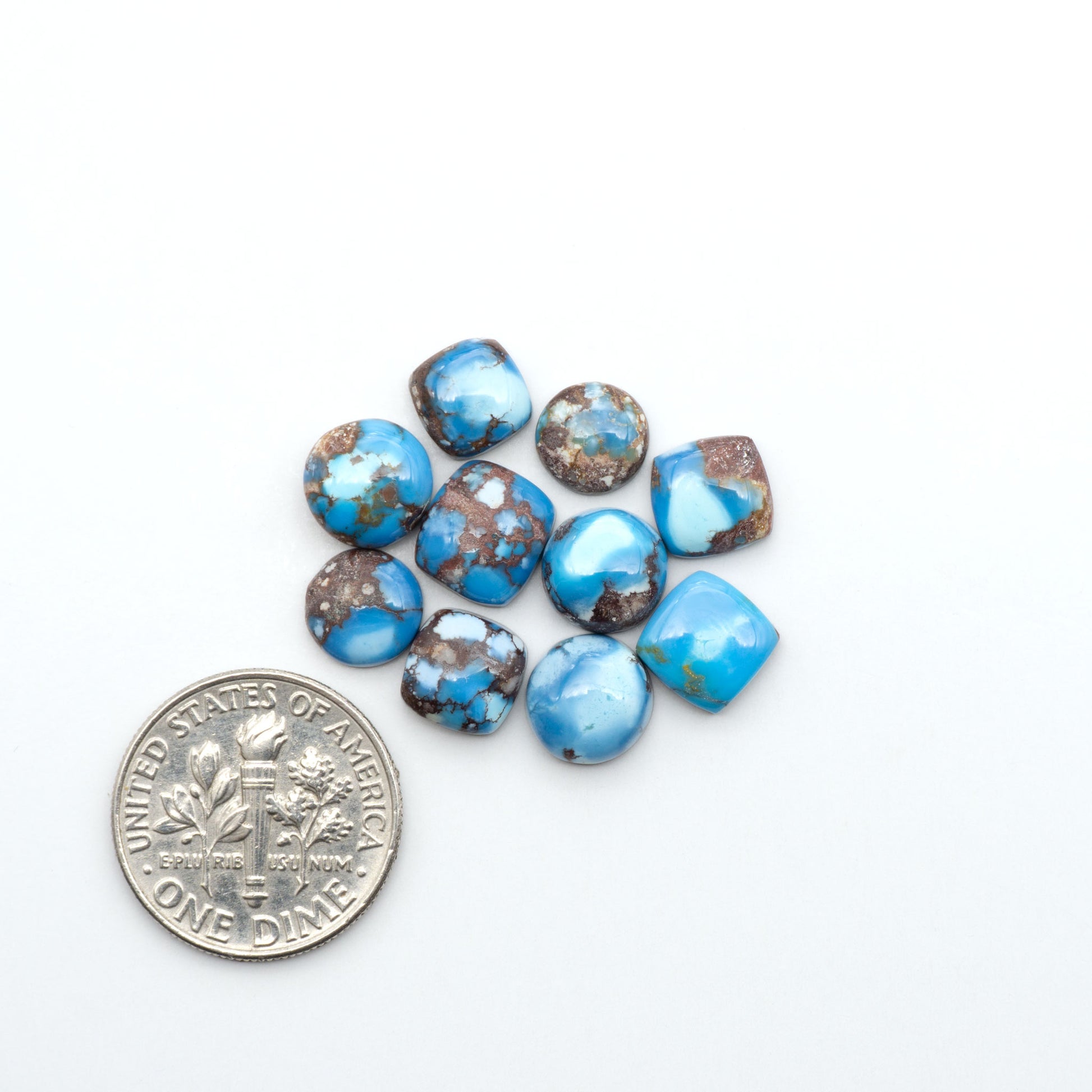 Golden Hills Turquoise cabochons, icy blue to lavender tones with chocolate matrix, polished stones on a white background with a US dime for scale