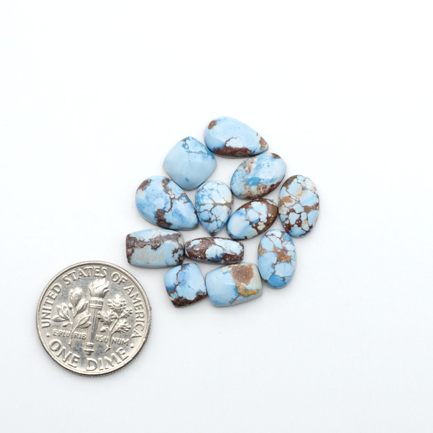 Golden Hills Turquoise cabochons, icy blue to lavender tones with chocolate matrix, polished stones on a white background with a US dime for scale