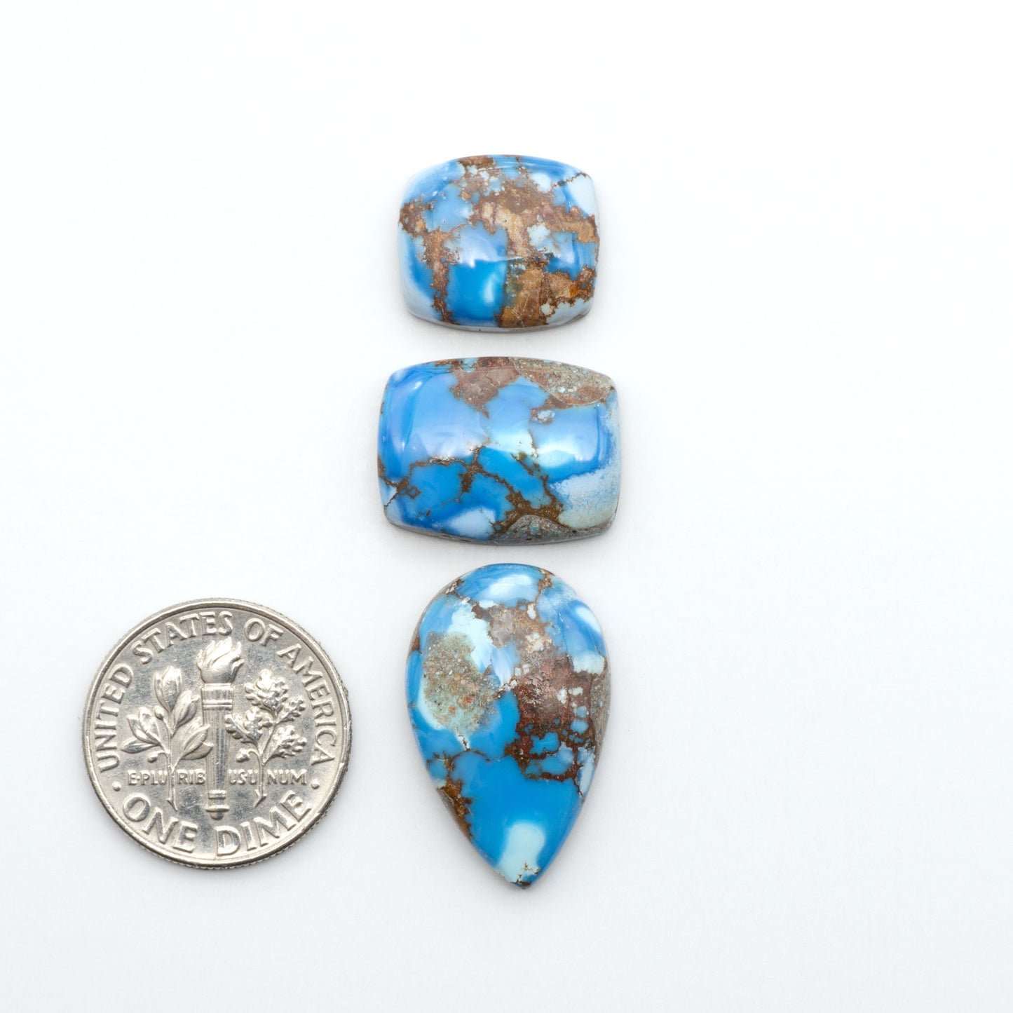 Golden Hills Turquoise cabochons, icy blue to lavender tones with chocolate matrix, polished stones on a white background with a US dime for scale