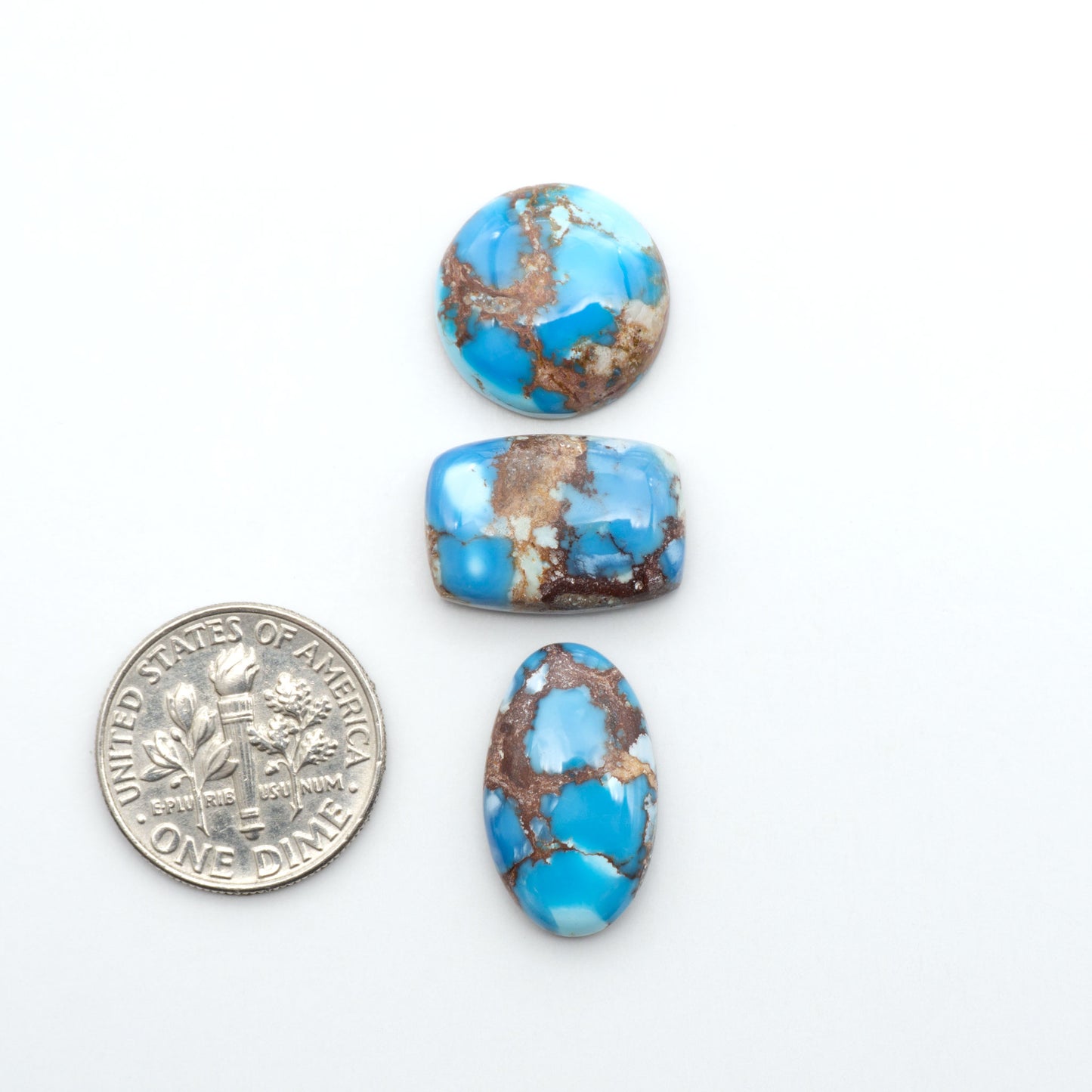 Golden Hills Turquoise cabochons, icy blue to lavender tones with chocolate matrix, polished stones on a white background with a US dime for scale