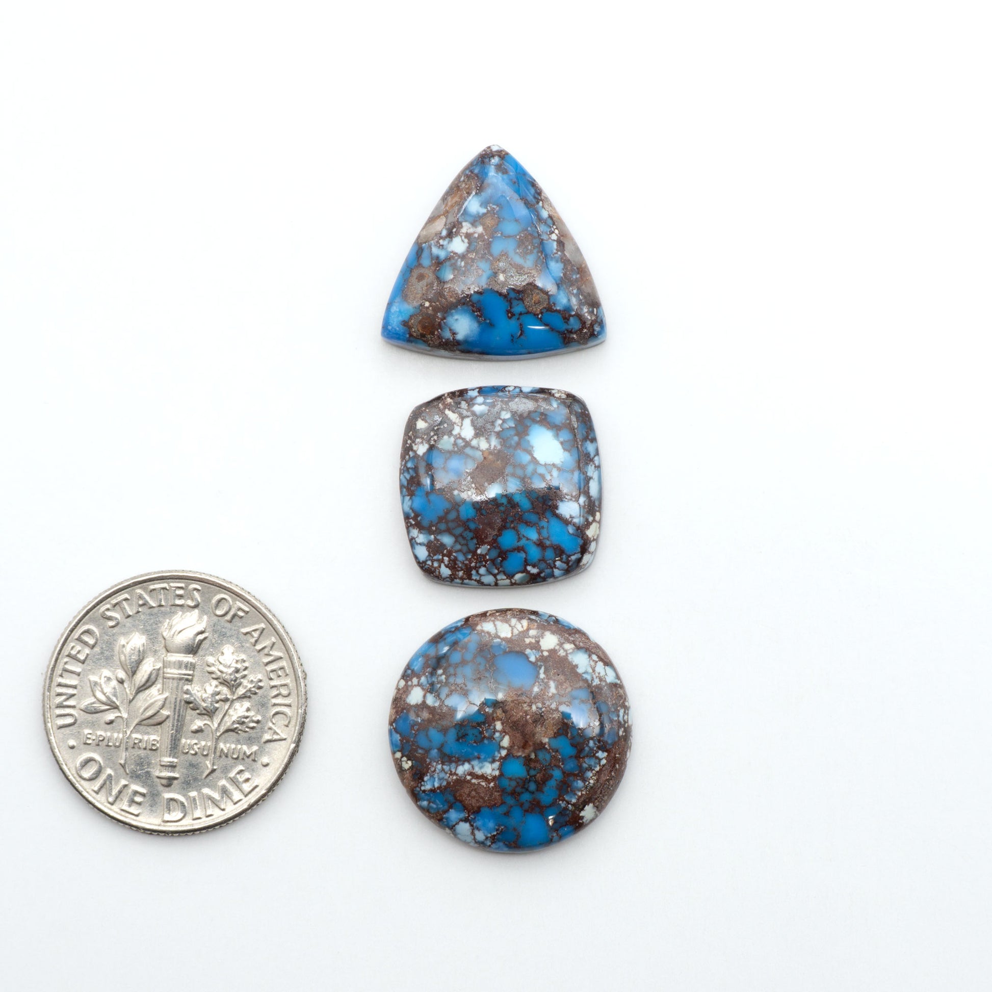 Golden Hills Turquoise cabochons, icy blue to lavender tones with chocolate matrix, polished stones on a white background with a US dime for scale