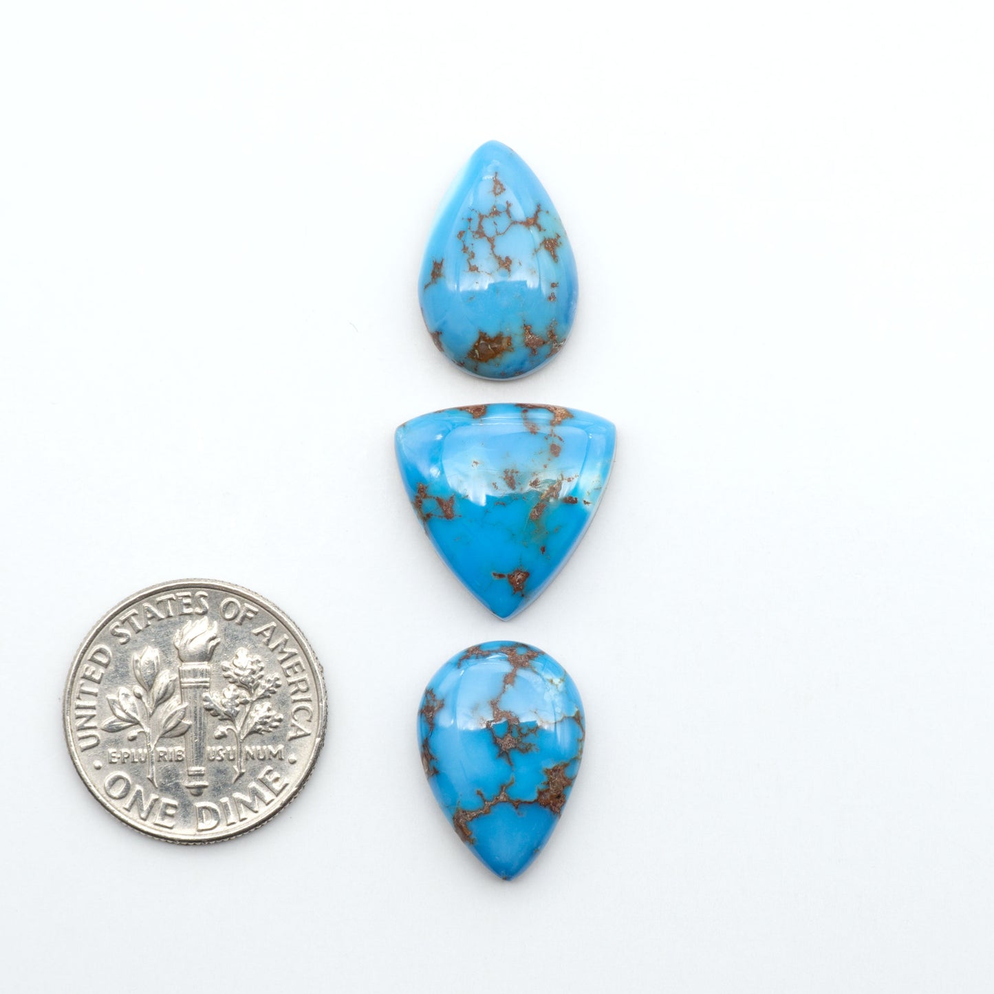 Golden Hills Turquoise cabochons, icy blue to lavender tones with chocolate matrix, polished stones on a white background with a US dime for scale
